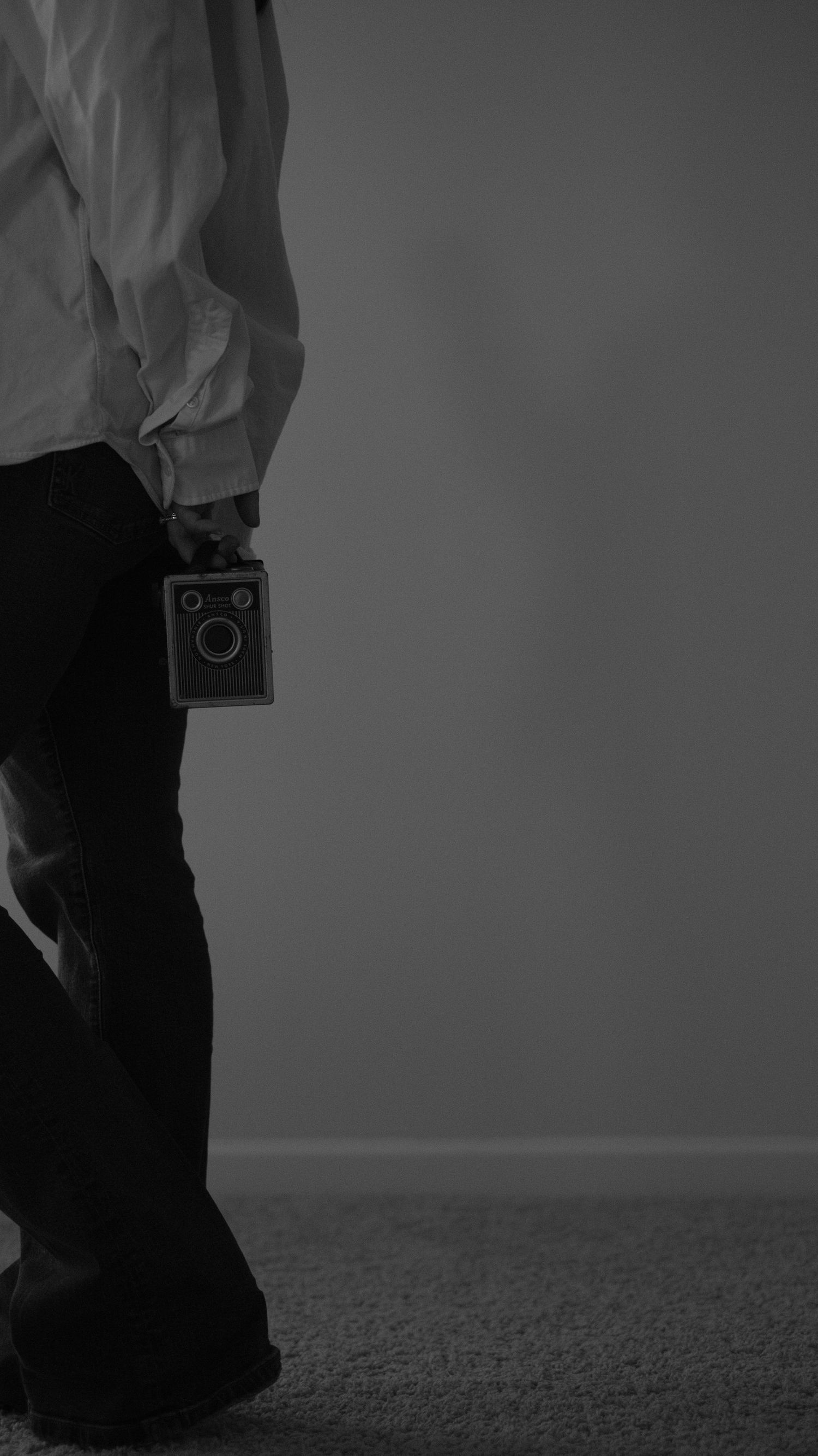 Black and white minimalist photo of person holding vintage camera.
