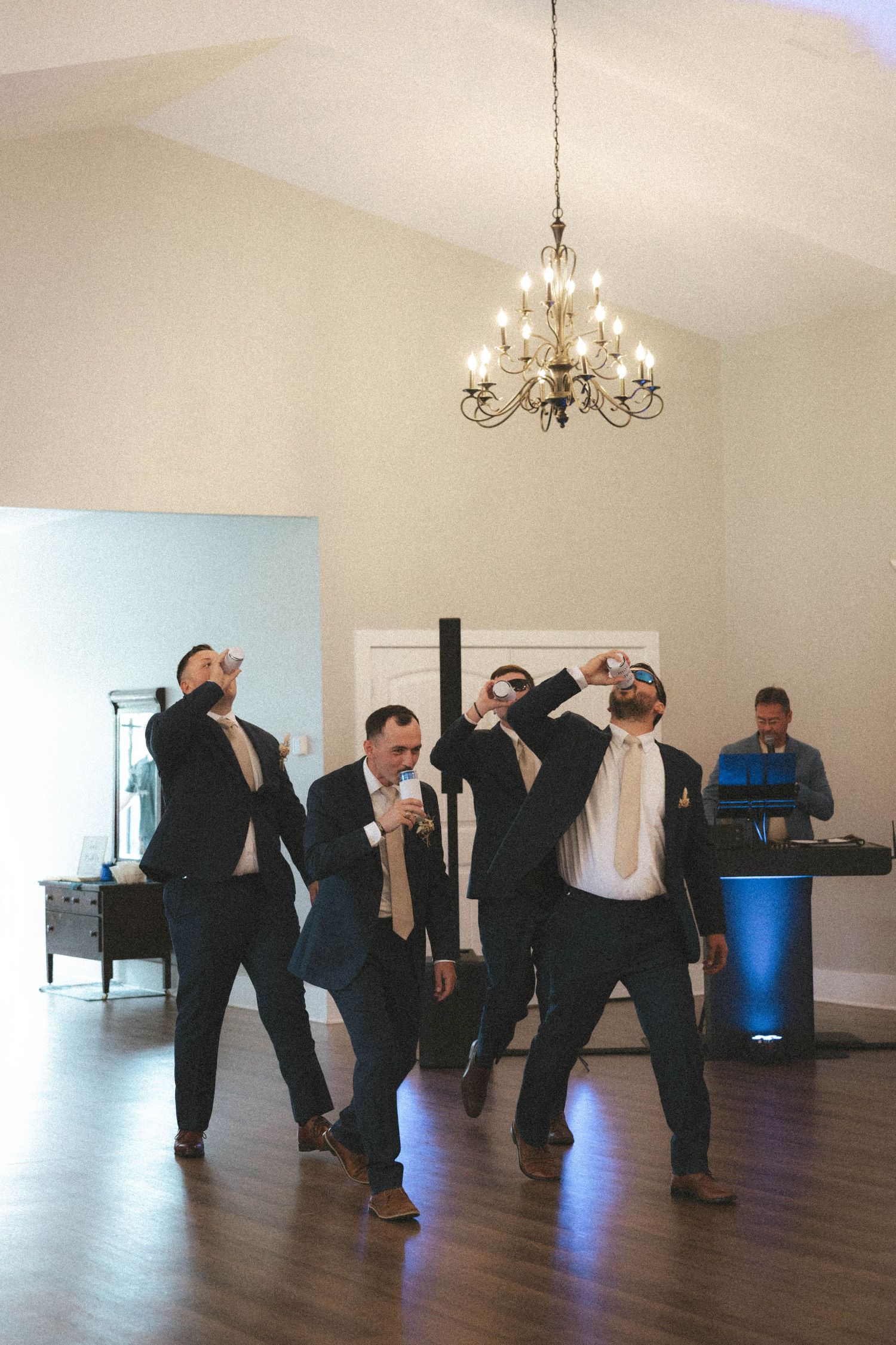 Groomsmen in navy suits celebrate with shots on the dance floor at a wedding reception.