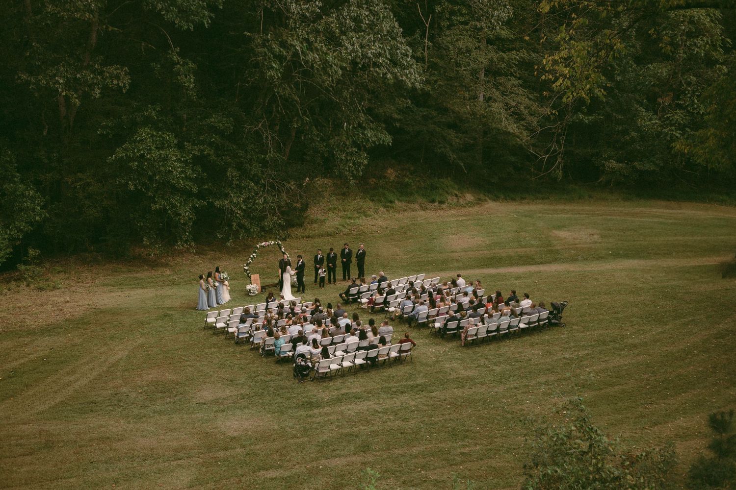 Aerial view of an outdoor wedding ceremony with guests seated in a U-shaped arrangement.