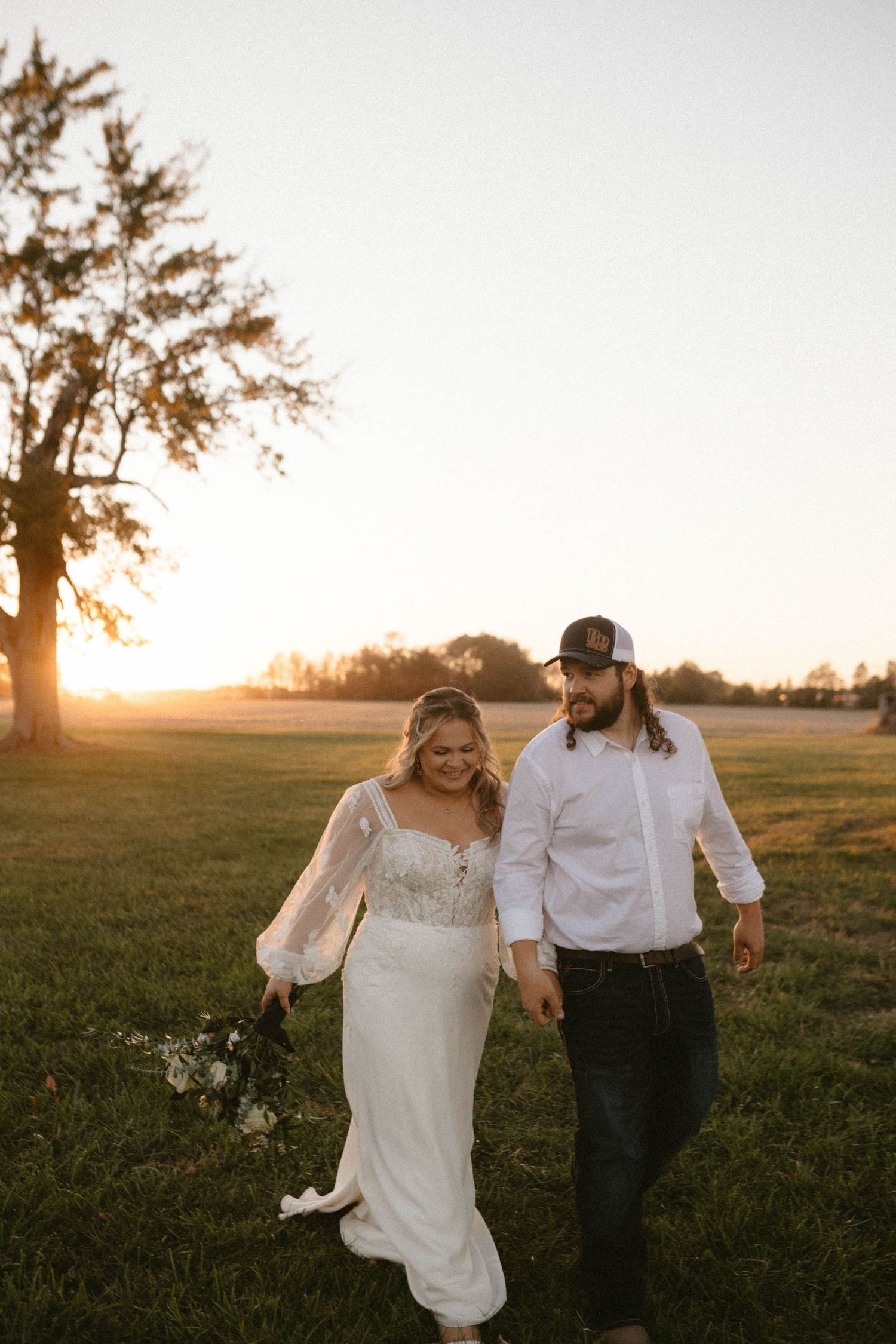 Couple walking through a golden sunset field in wedding attire.