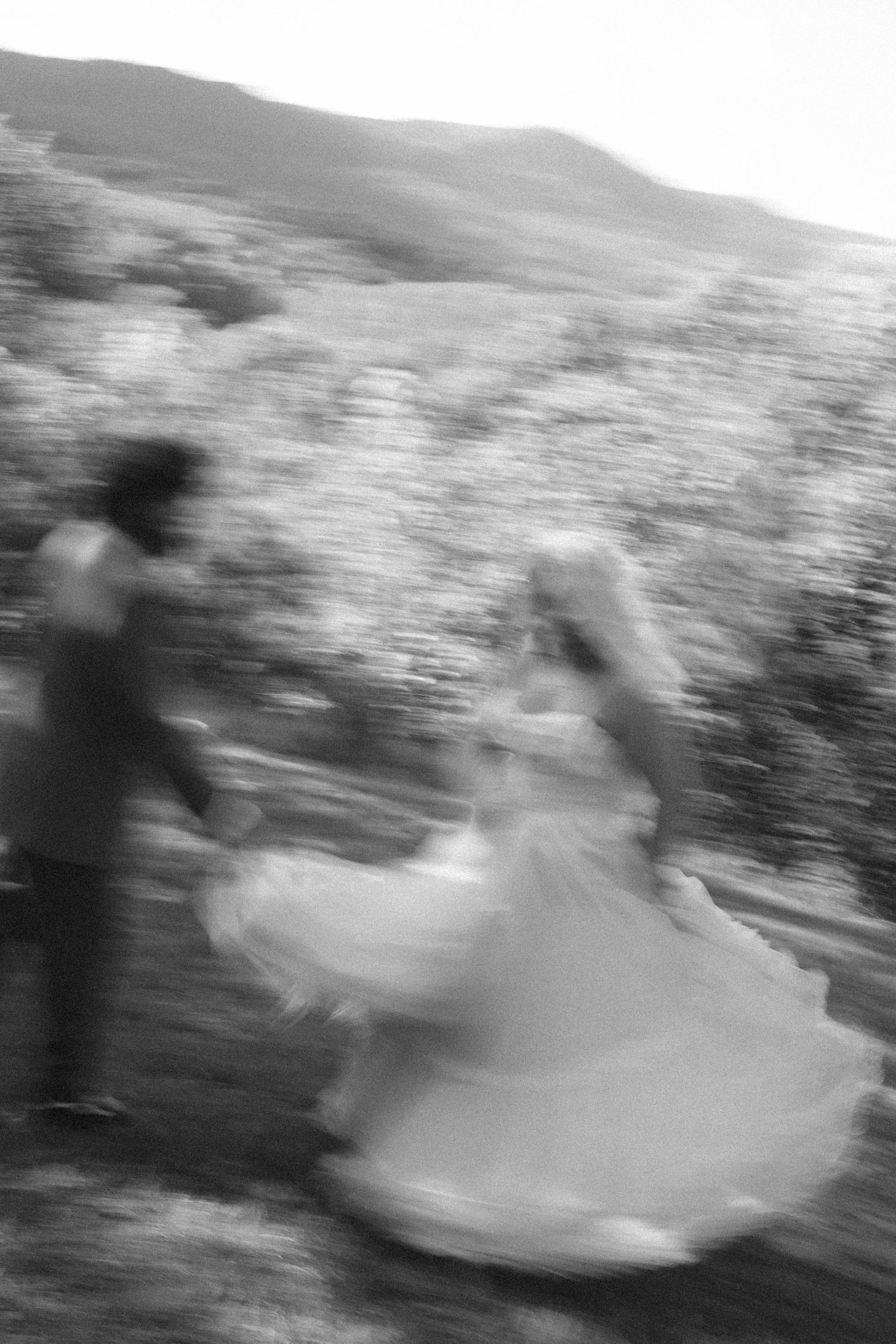 Blurred black and white photo of a bride and groom dancing outdoors with mountains in the background.
