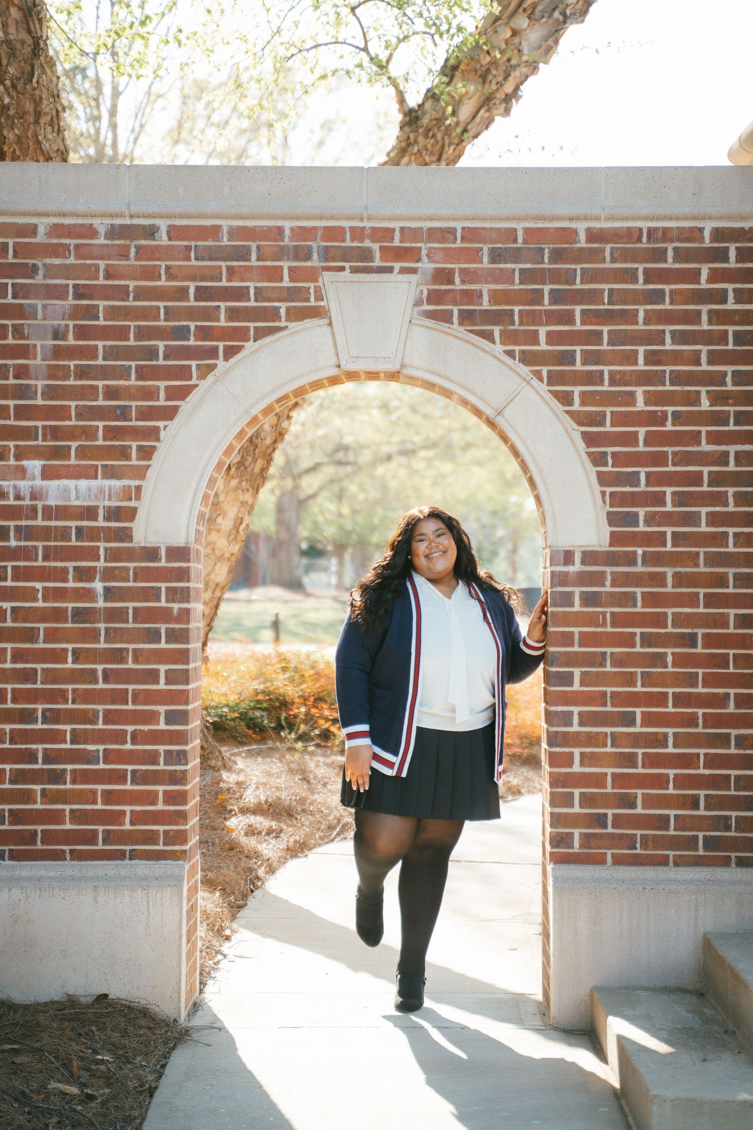 Joyful graduation photos taken through a brick archway on a sunny day.