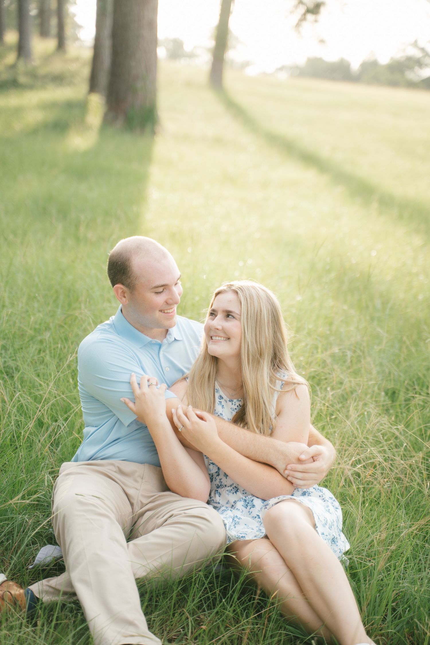 Couple sharing joyful laughter while sitting in sunlit grass.