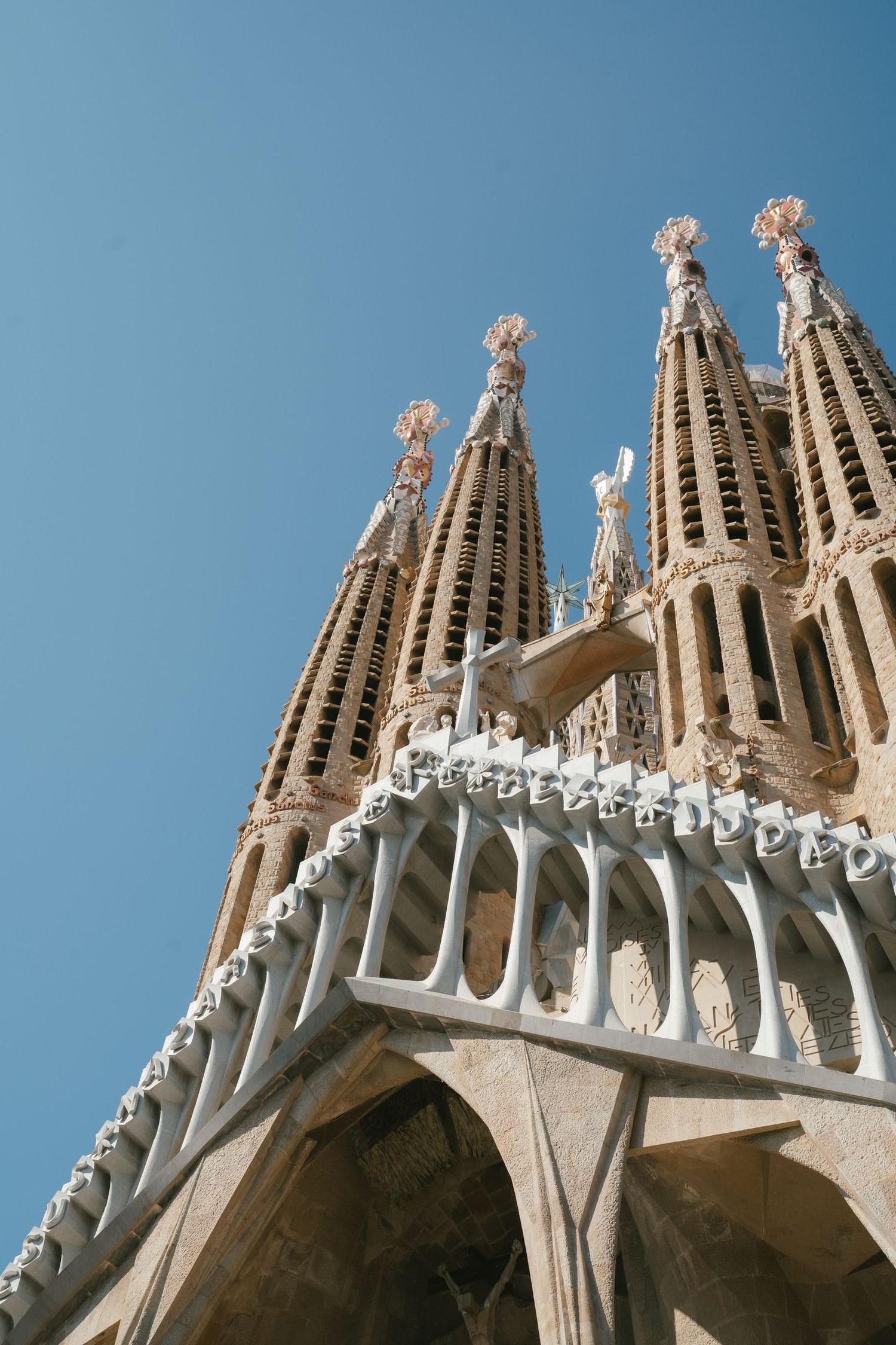 Architectural detail of the Sagrada Familia basilica spires and ornate stonework against blue sky in Barcelona, Spain.