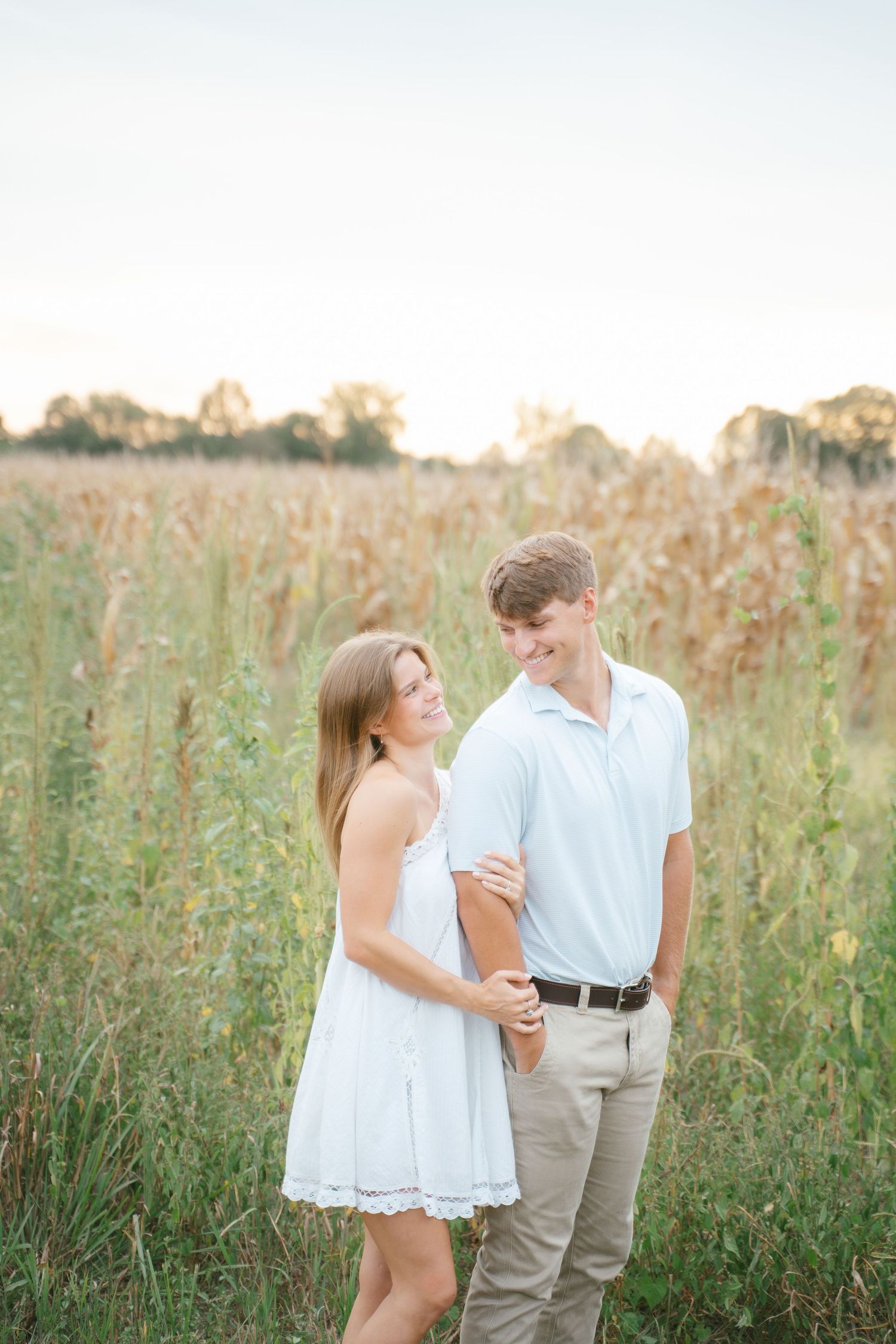 Couple shares a tender moment together in a sunlit field of tall grass and wildflowers.