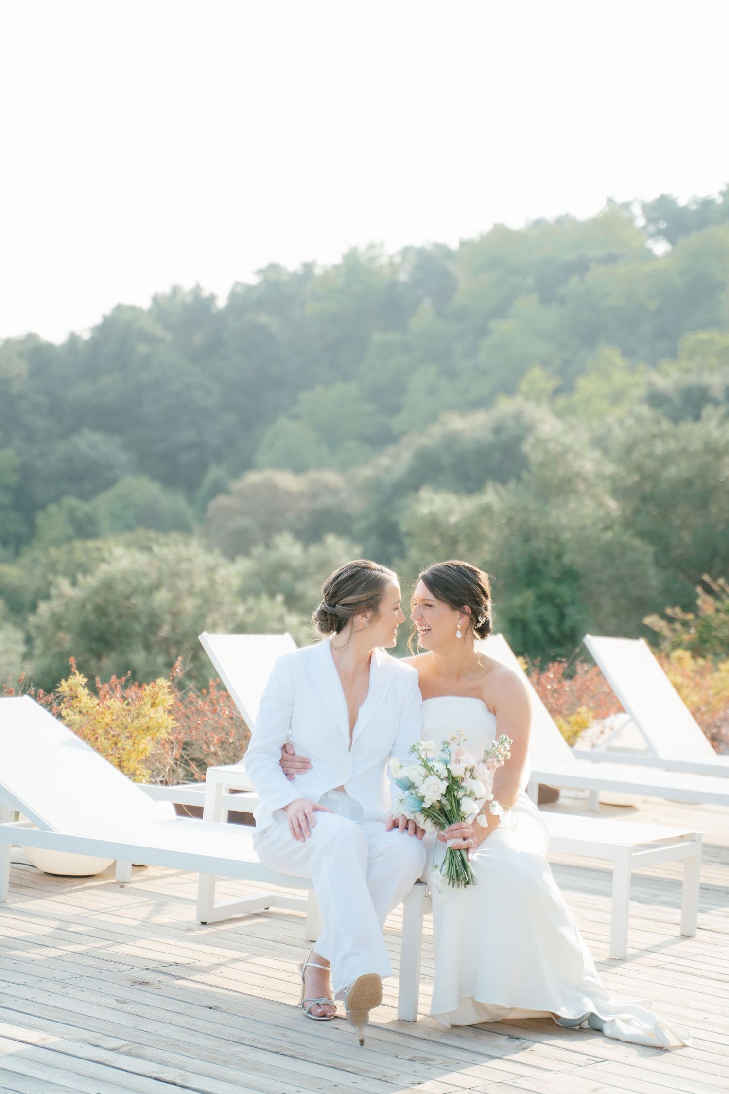 Romantic wedding couple relaxing on white lounge chairs at outdoor venue.