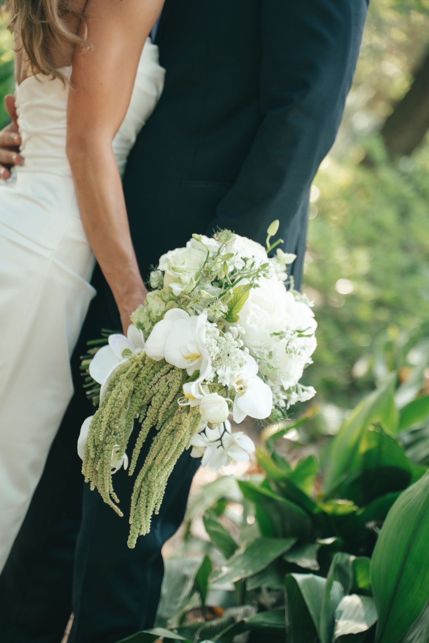 Bride and groom holding a white orchid and greenery wedding bouquet with trailing amaranthus outdoors.