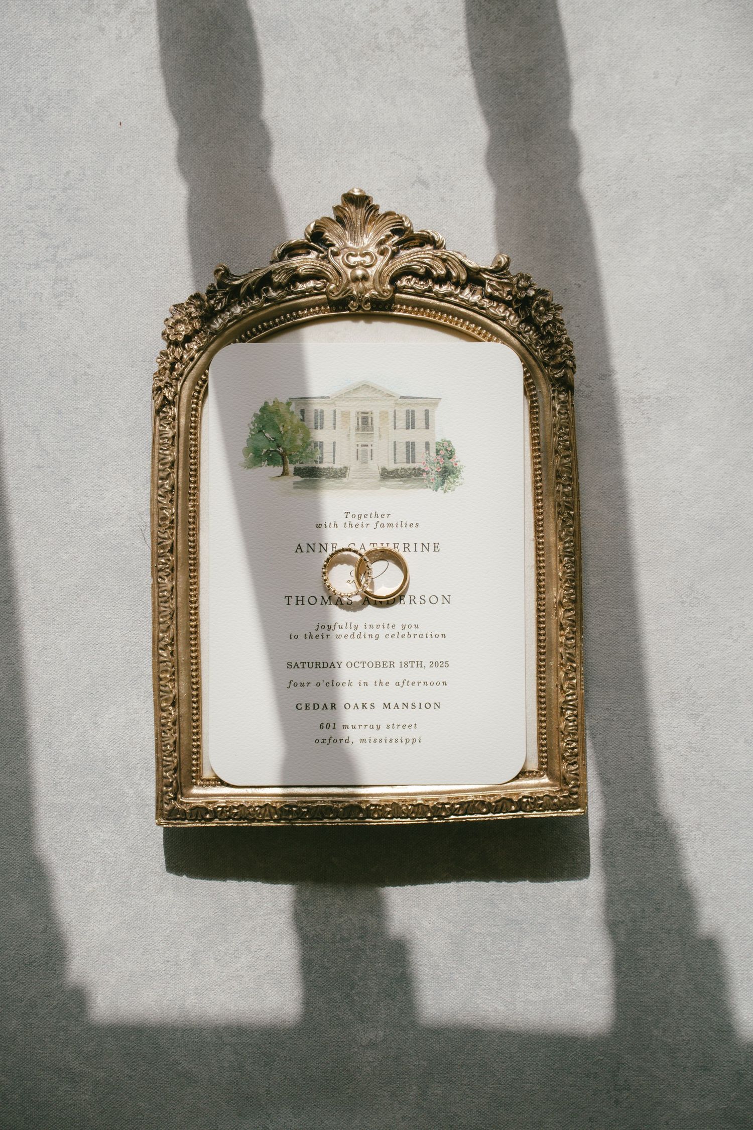 Wedding invitation in ornate gold frame with venue illustration and ring details.