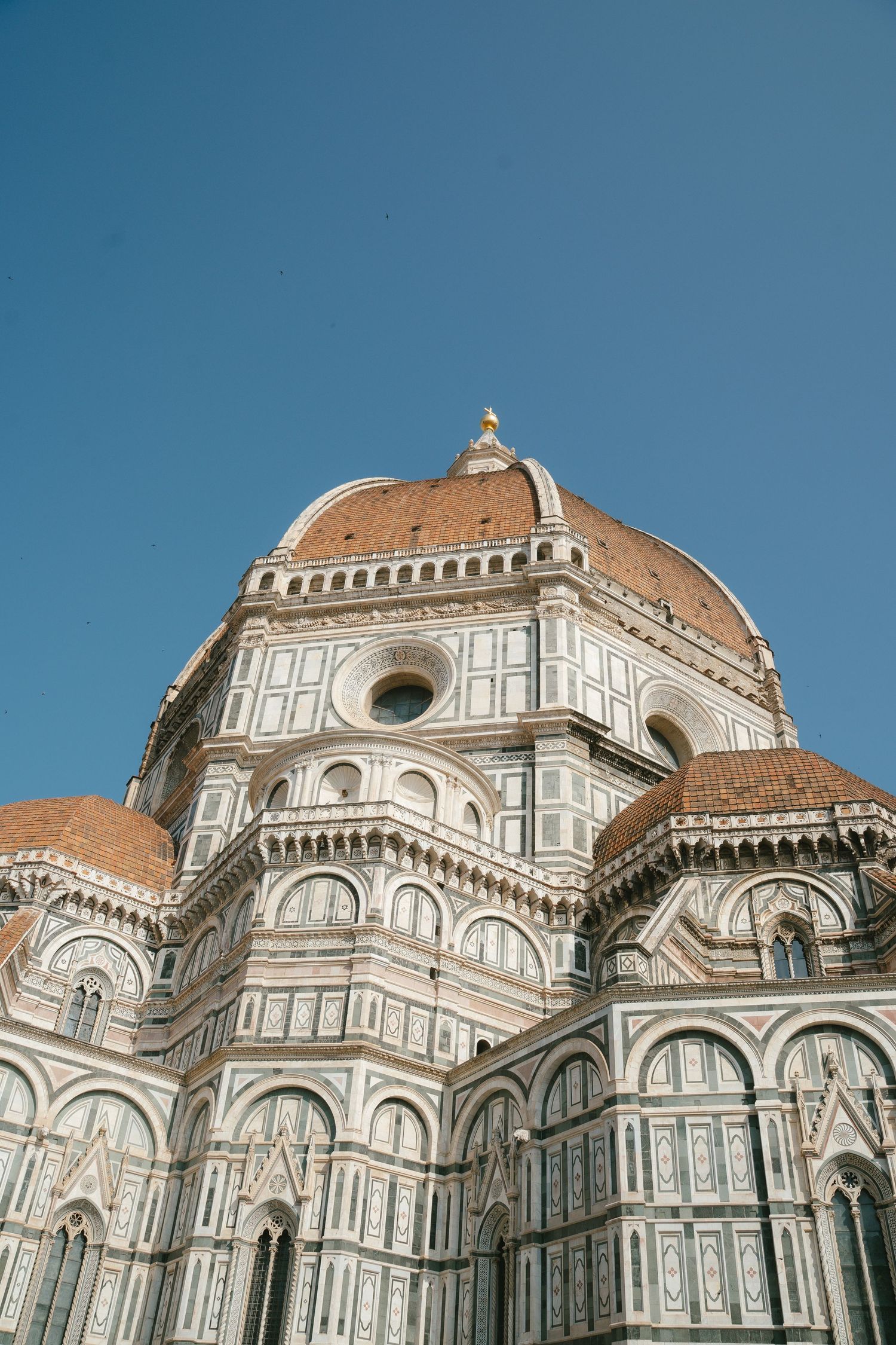 Architectural details of Florence Cathedral's iconic dome and marble facade against blue sky in Italy.