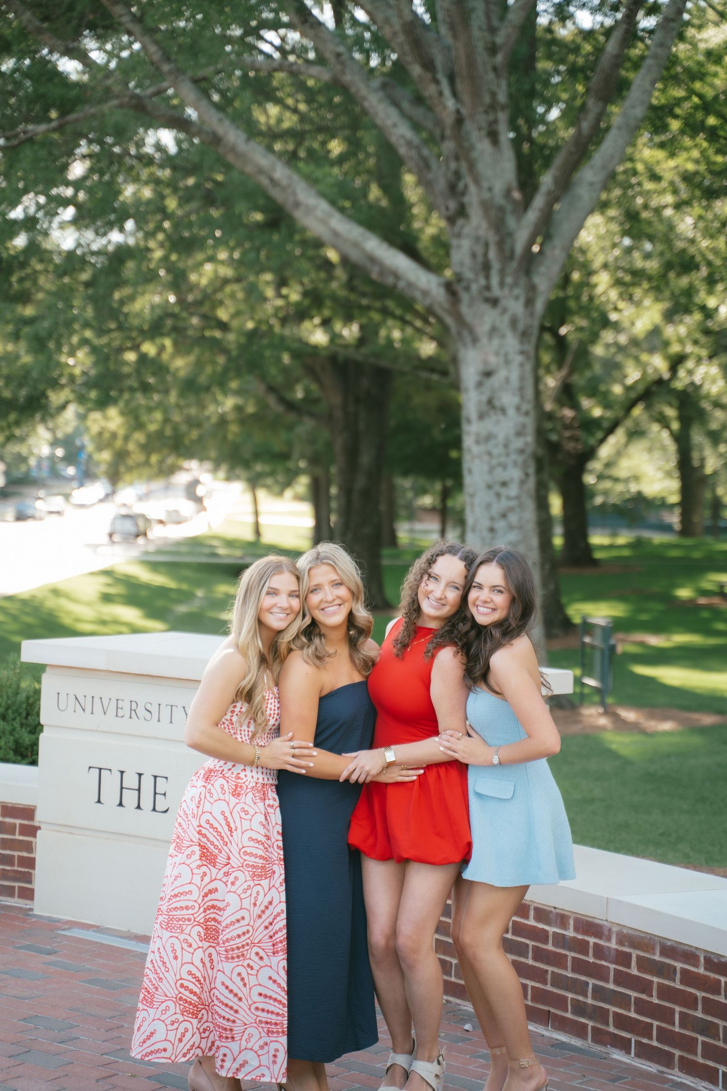 Group posing by university entrance sign on sunny campus grounds.