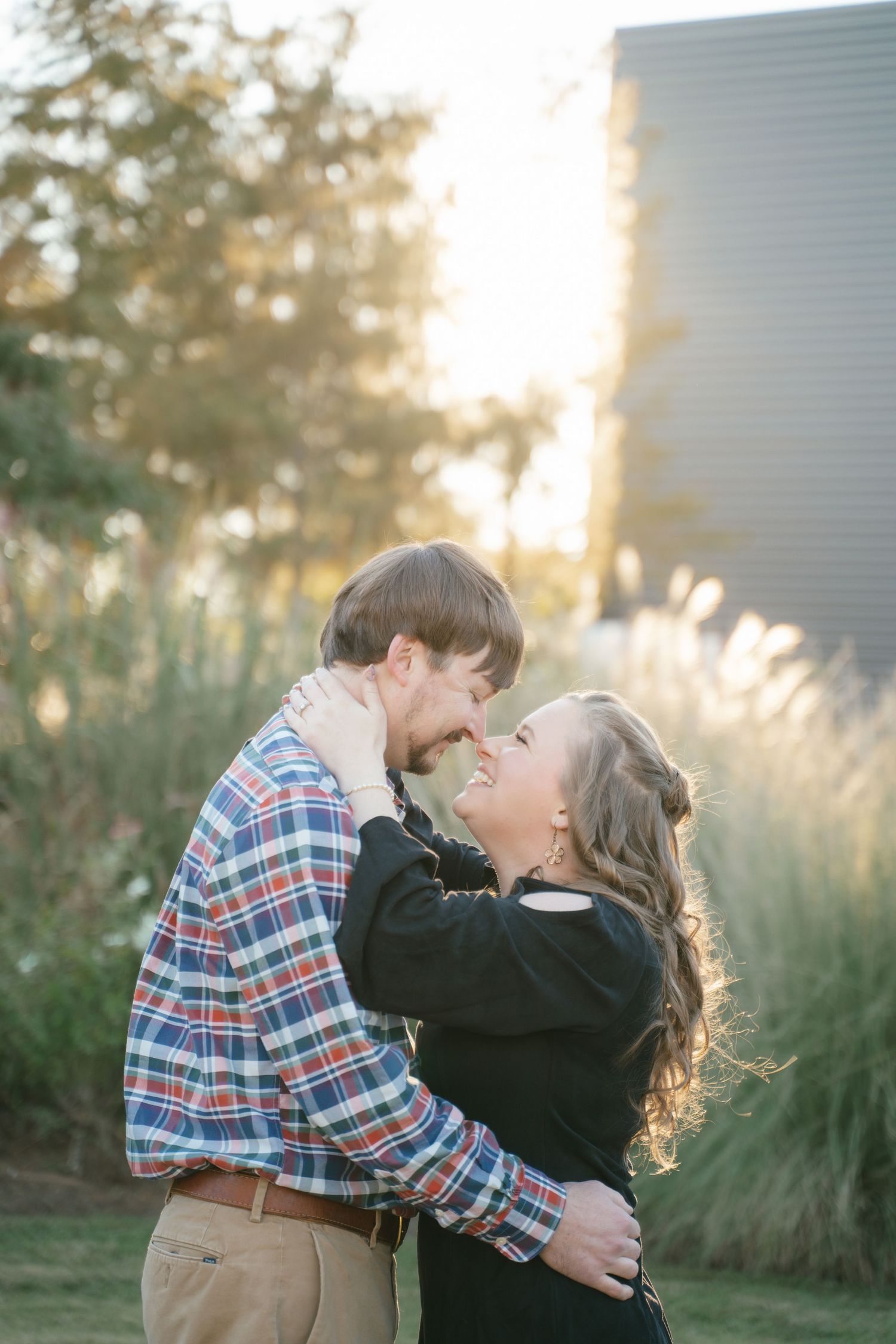 A couple embracing and kissing in front of tall ornamental grasses at sunset.
