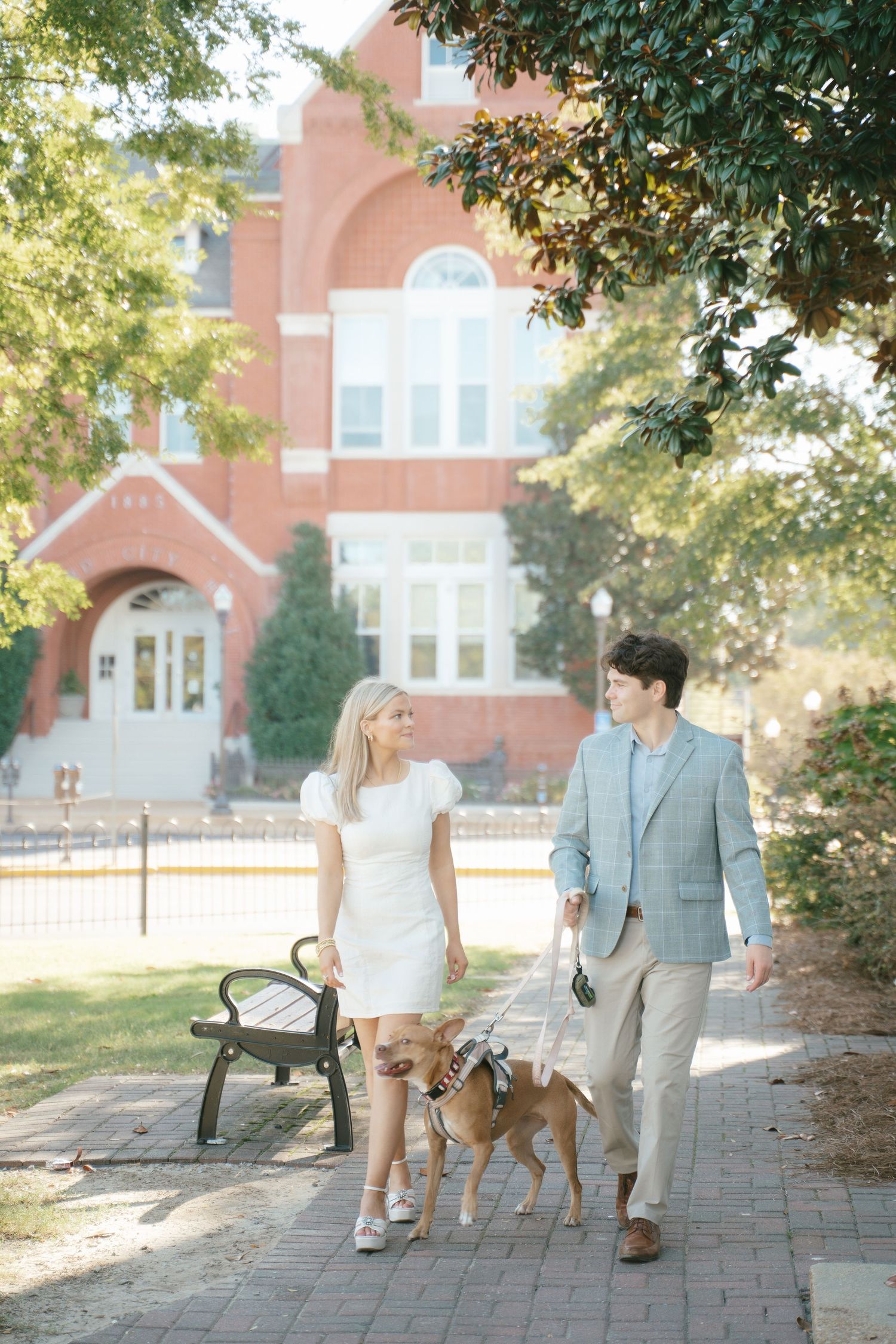 A couple walking their golden retriever on a brick path near a brick building.