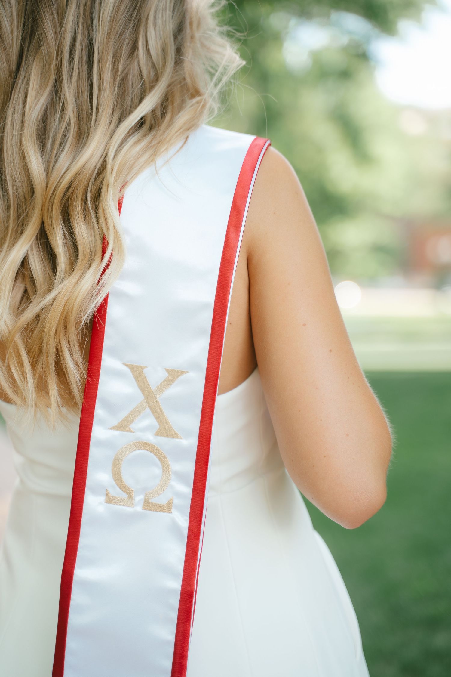 Detail shot of white graduation stole with Greek letters and red trim.