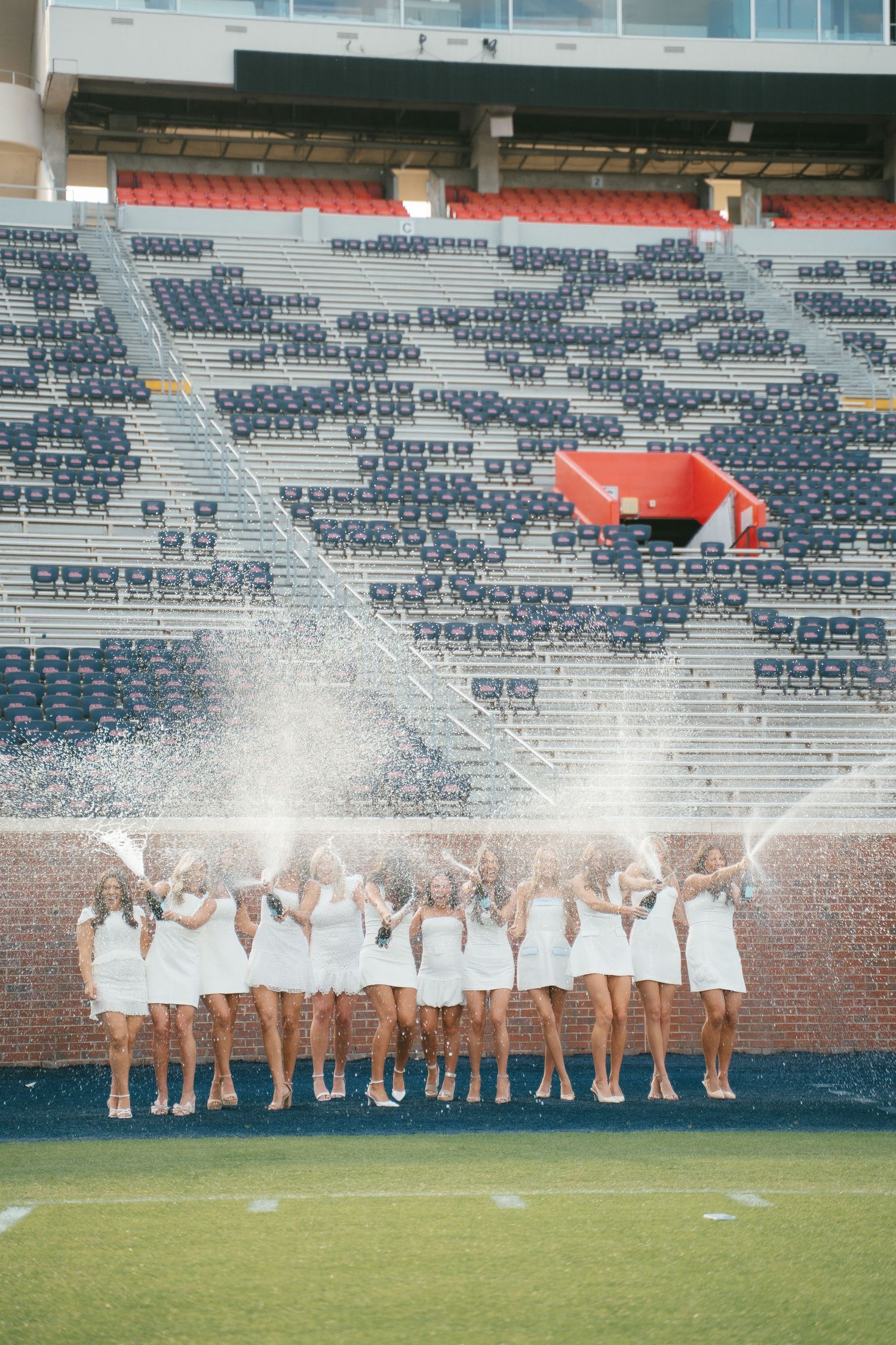 A group in white dresses creates a fun photo with water splashes at a football stadium.