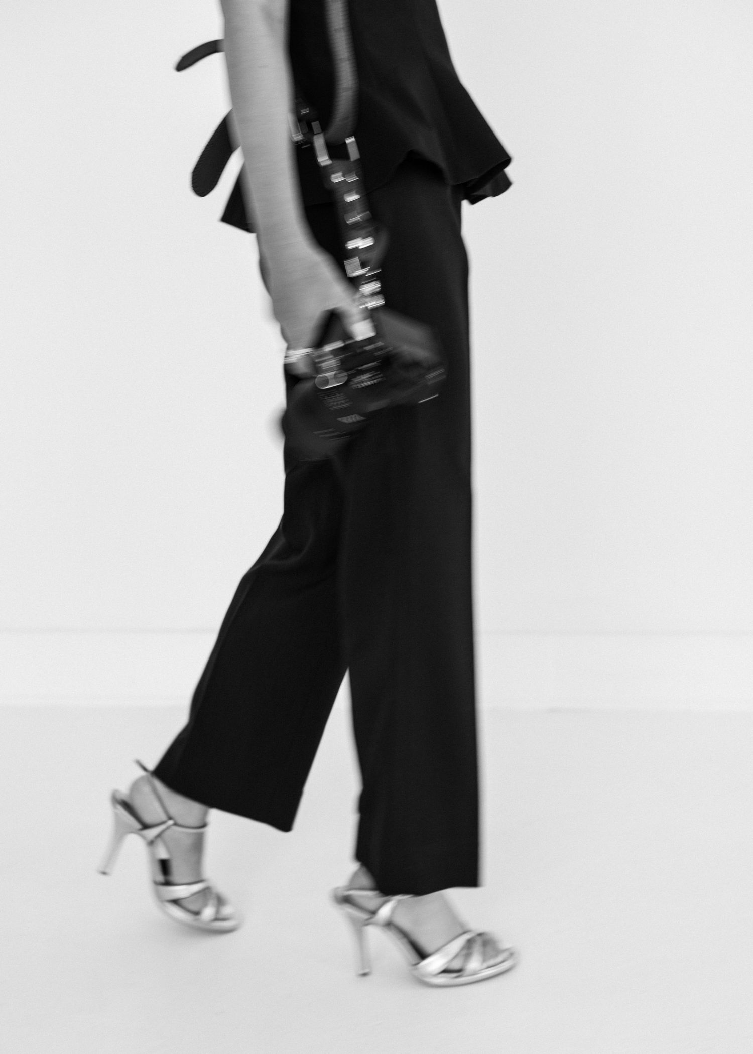 Close-up view of elegant black pants and silver high heels walking on white background.