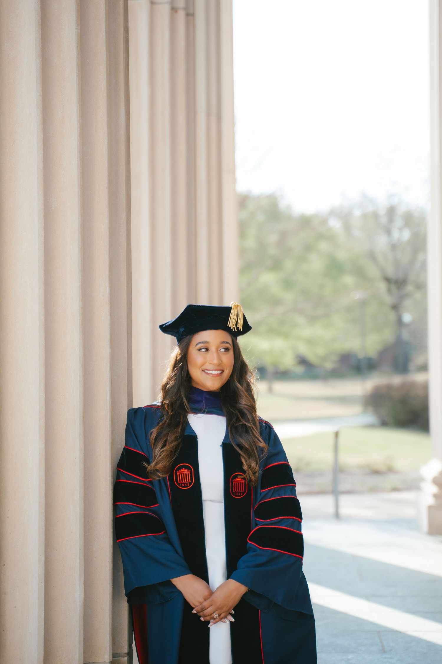 Academic wearing traditional graduation regalia and cap in front of light curtains.