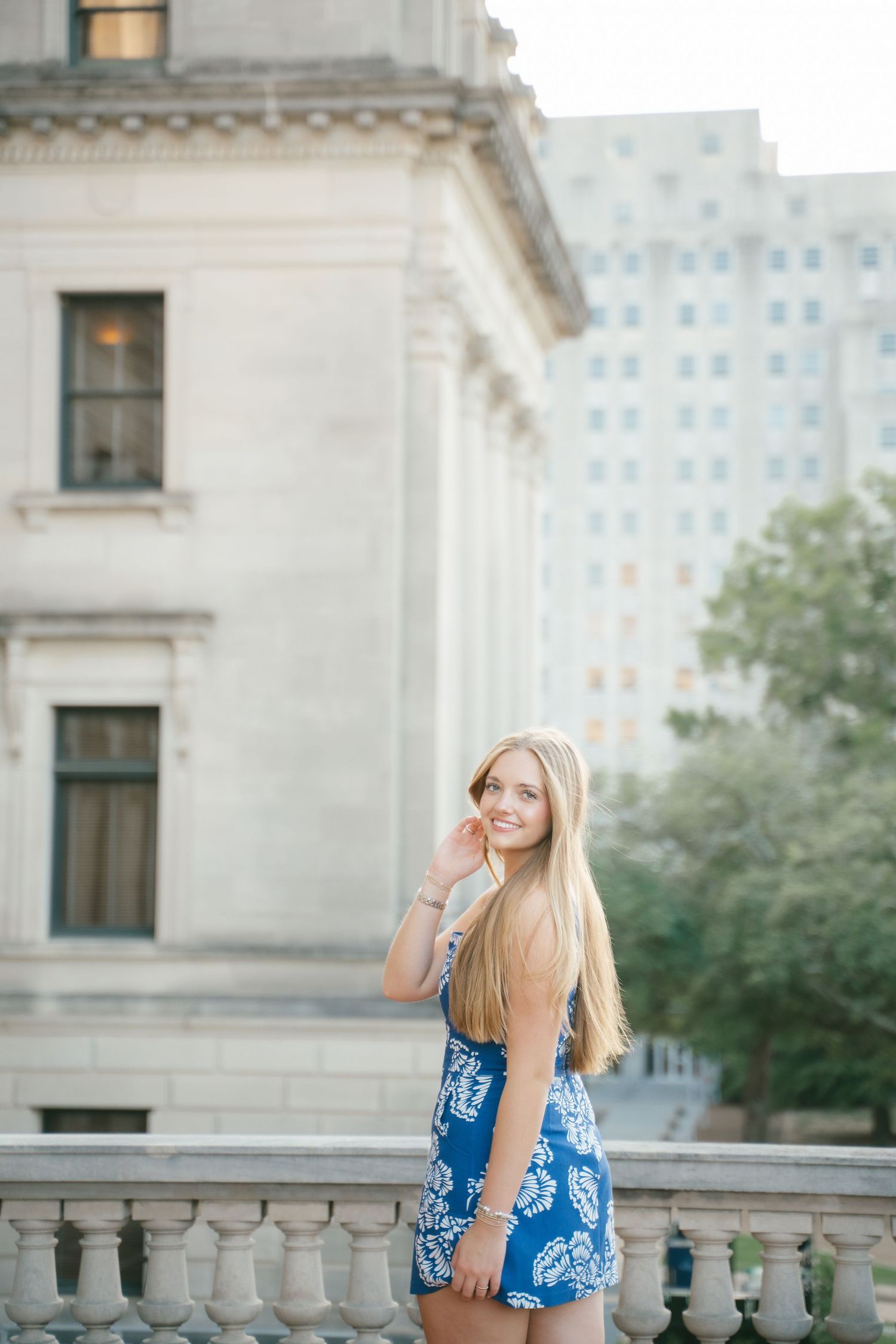 Person in blue patterned dress posing near classical building architecture.