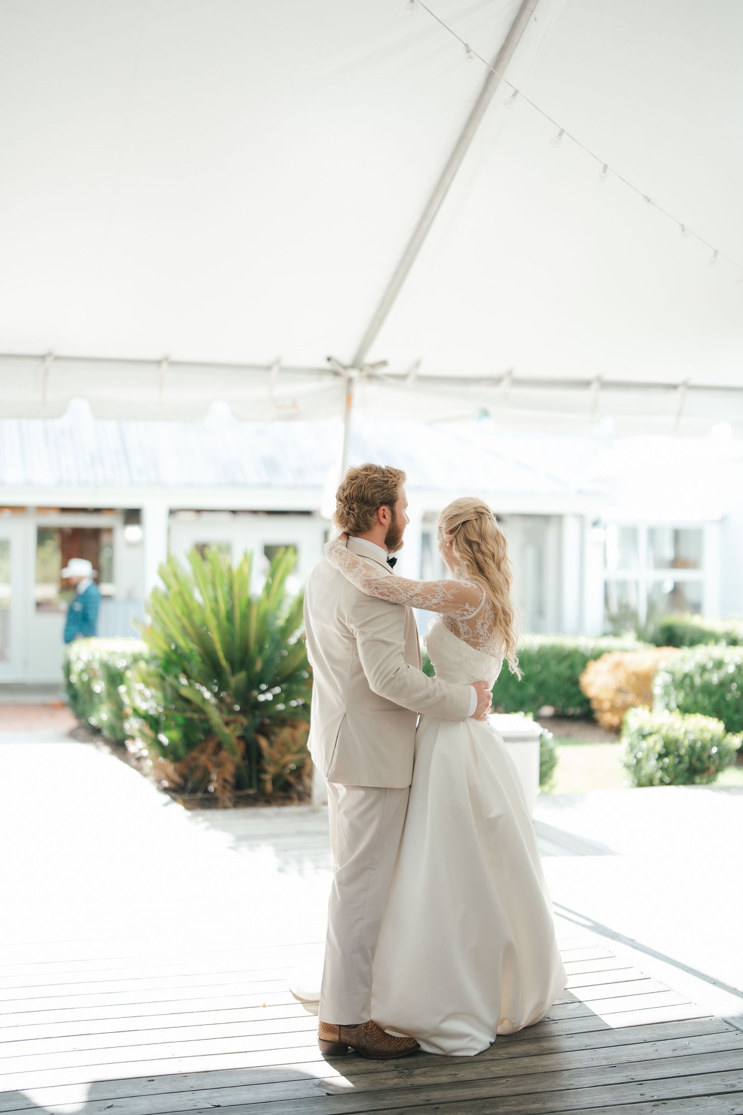 Bride and groom share first dance under white tent at outdoor wedding reception with tropical greenery backdrop.