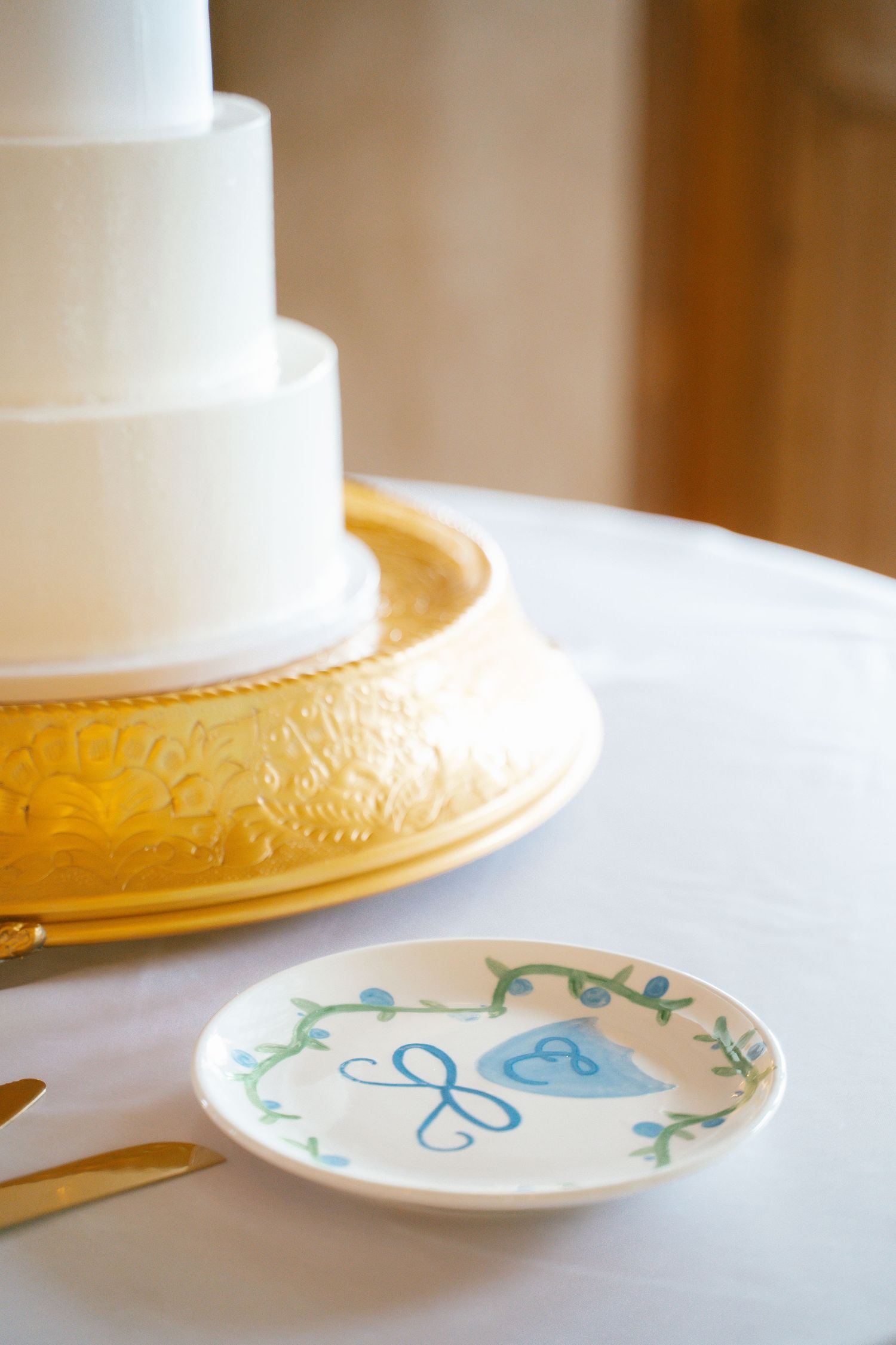 Elegant white wedding cake displayed on a gold charger plate with decorative dishes.