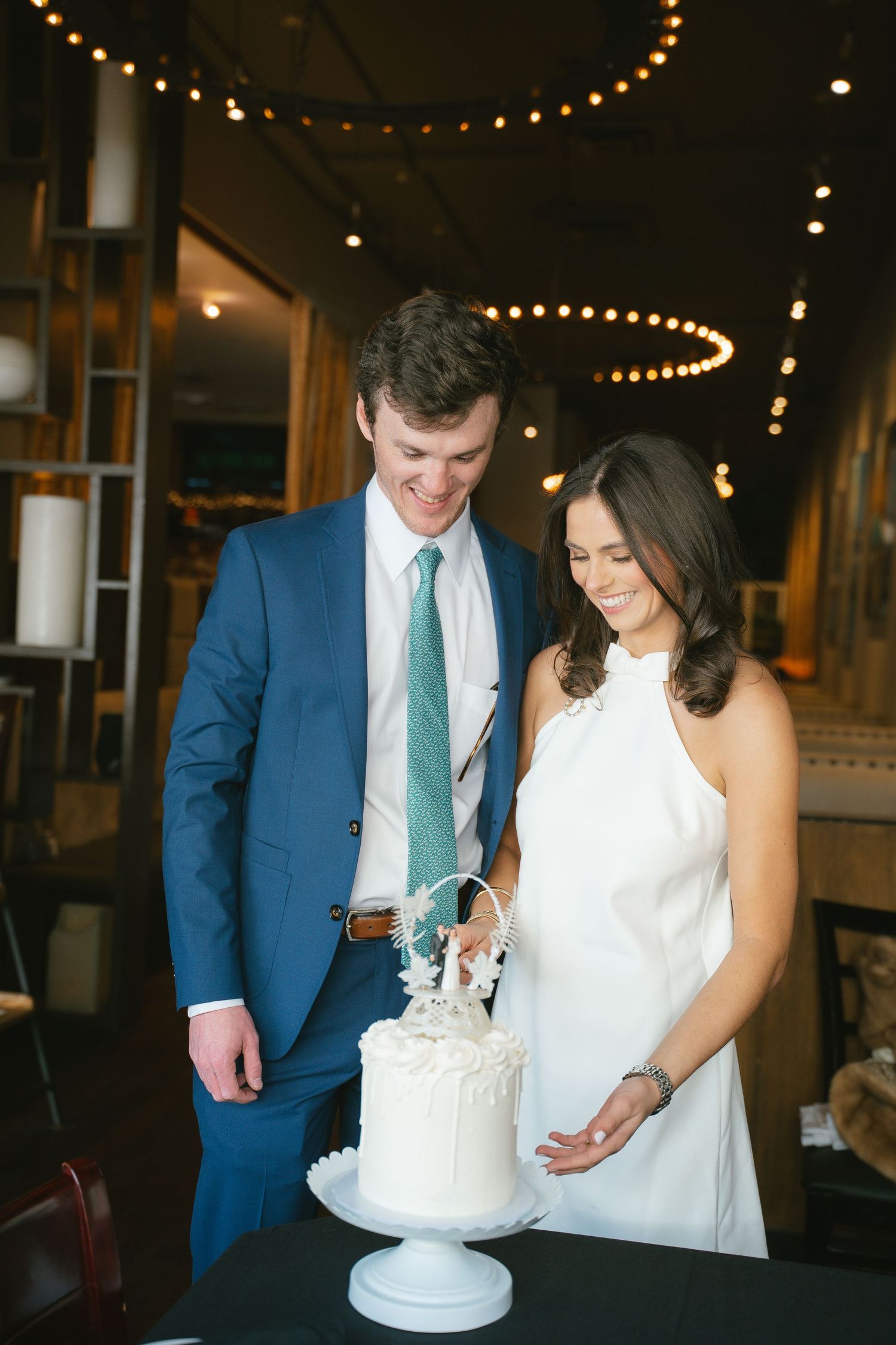 Couple cutting their wedding cake under string lights at reception.
