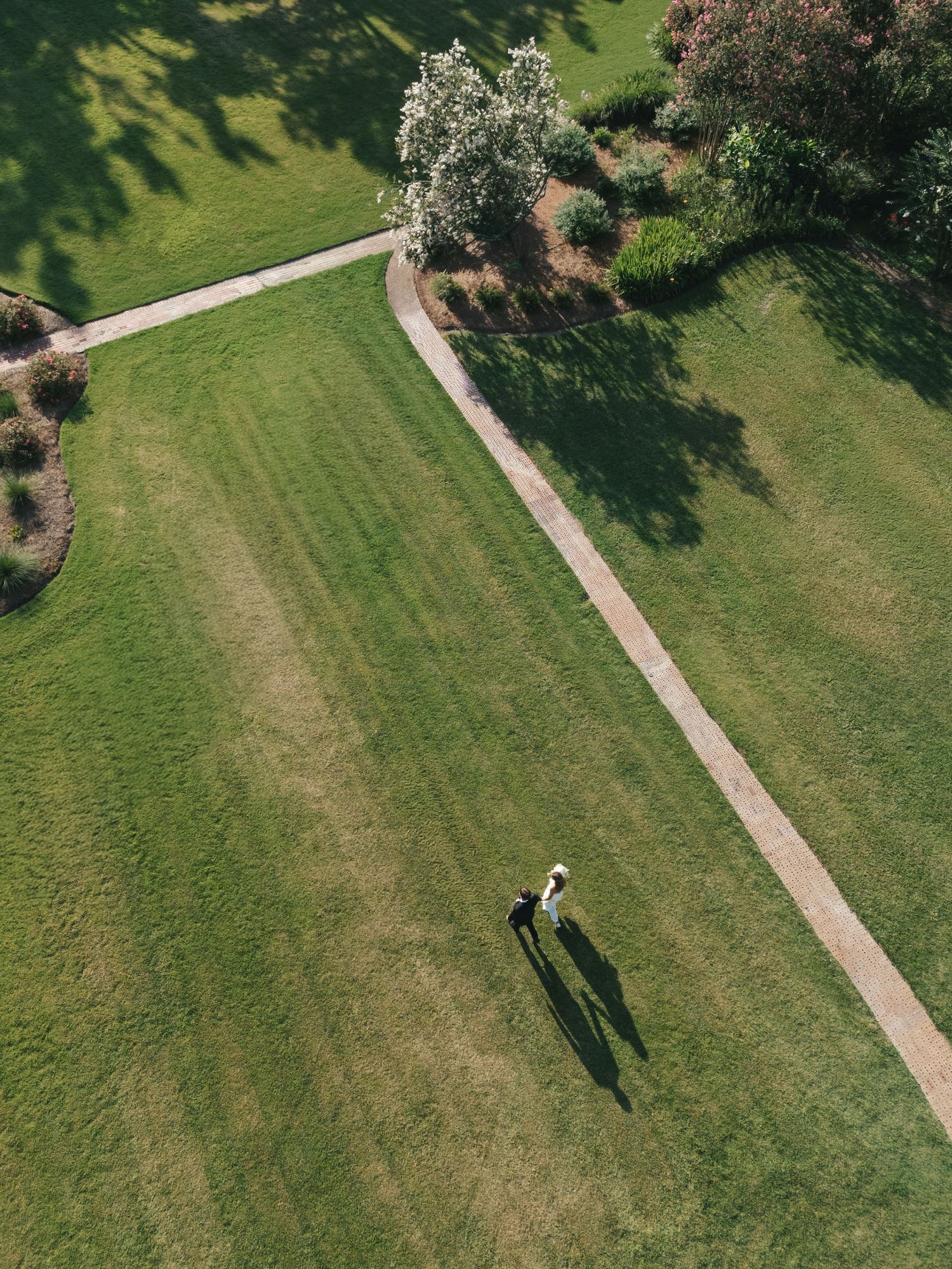 Aerial view of two people walking on a curved path through a lush green park with trees and manicured lawns.