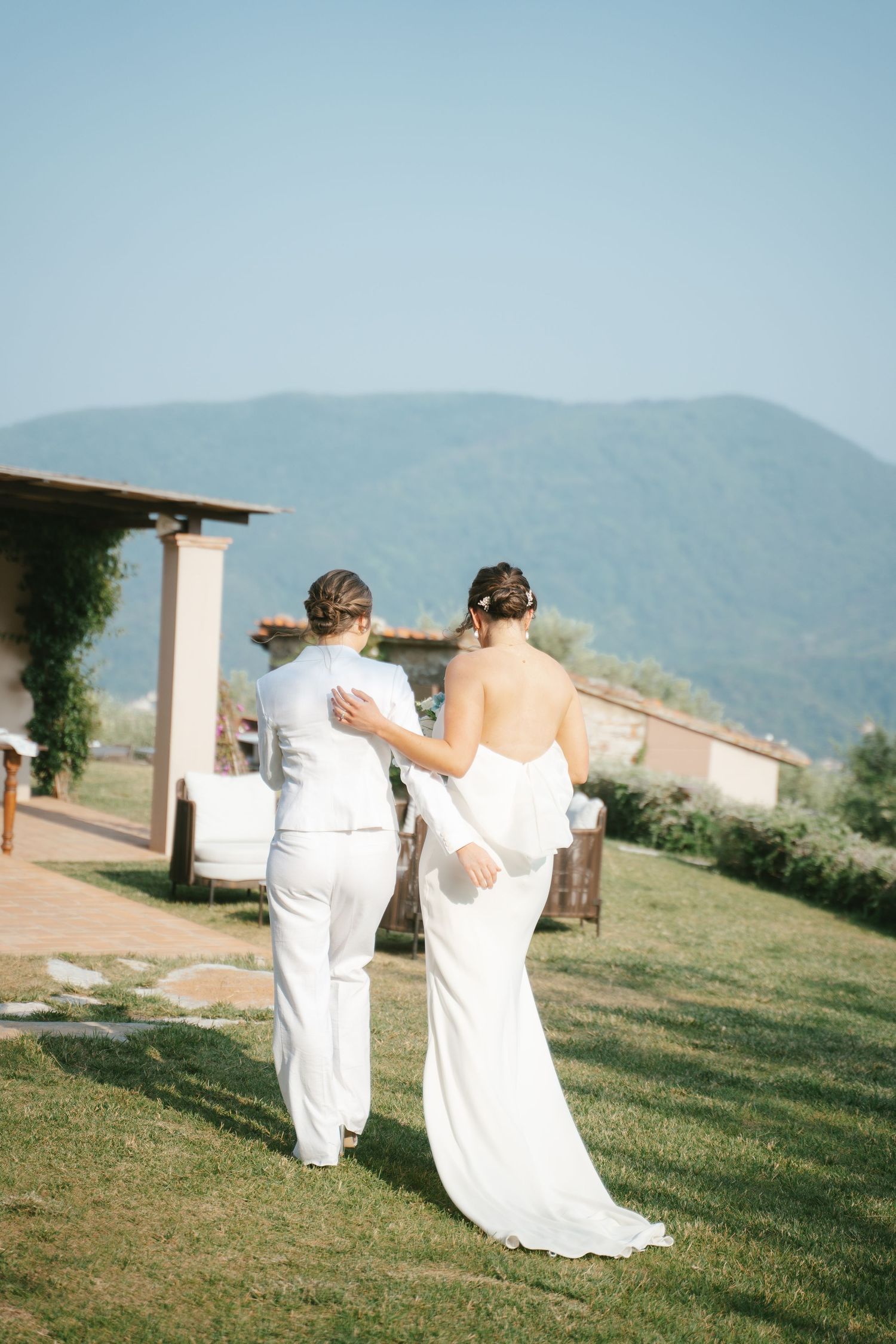 Two people in white walking together on a path with mountain views in the background.