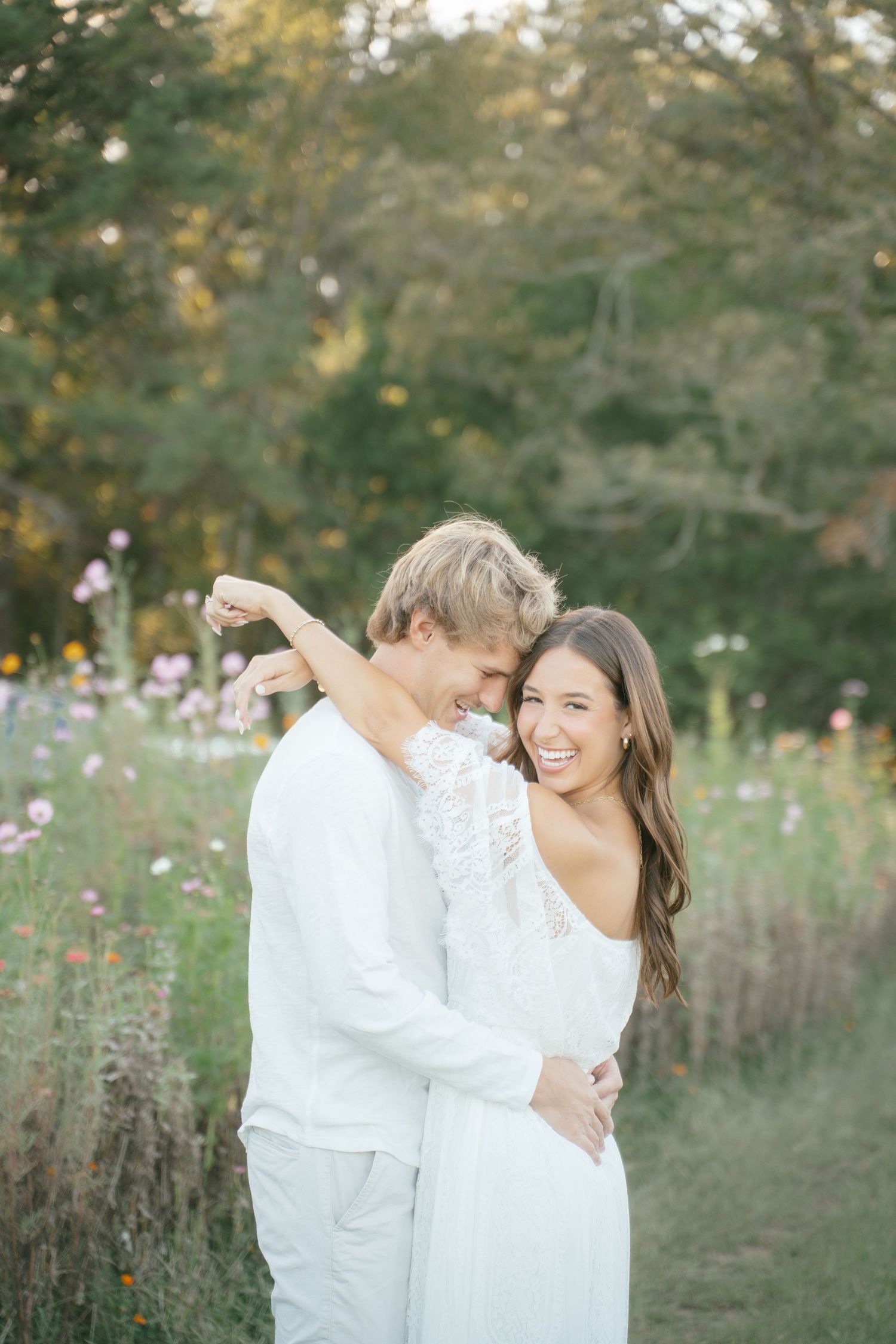 A couple wearing white clothing shares an intimate moment in a summer meadow.