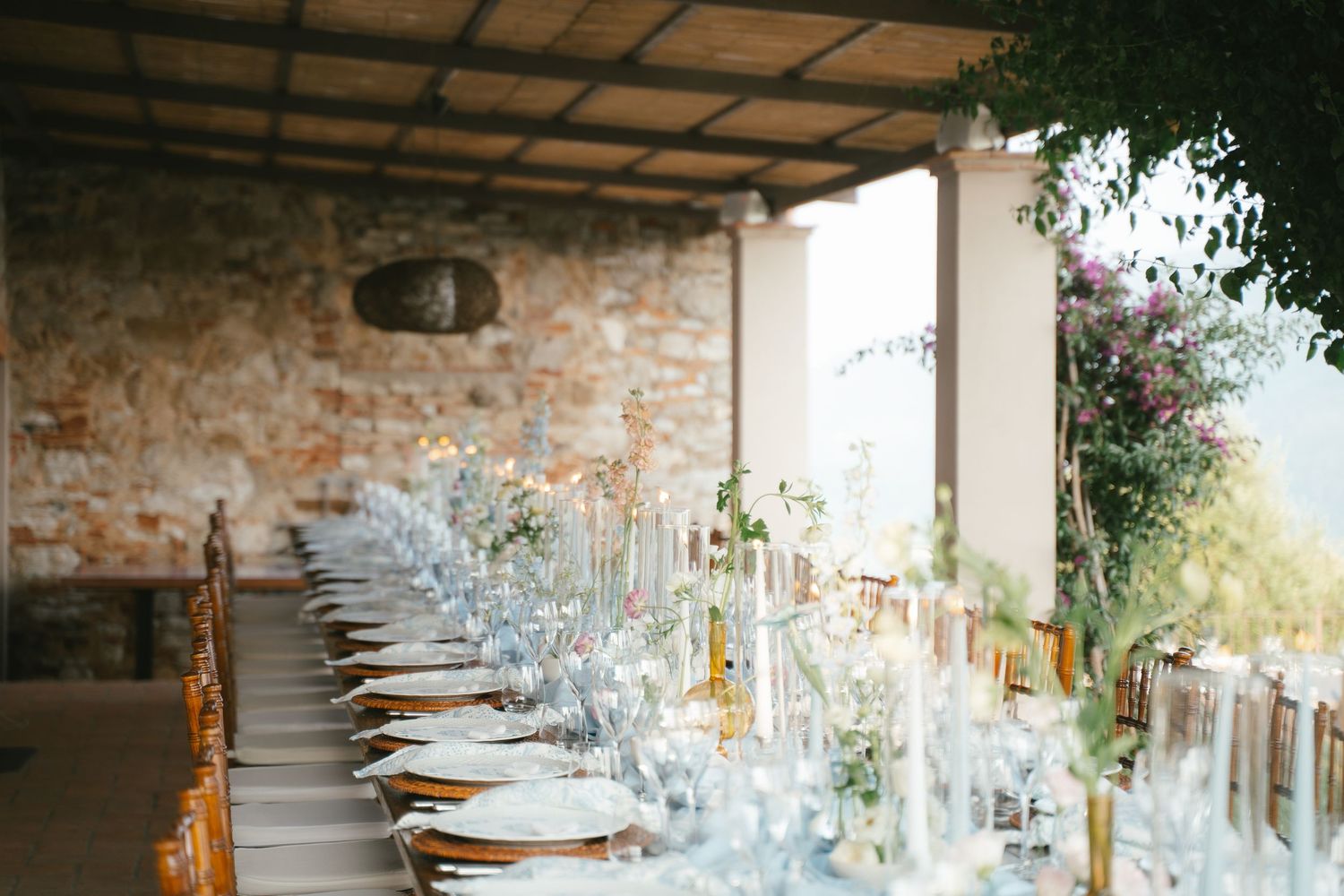 Long dining table set with crystal glasses and place settings under a covered outdoor venue.