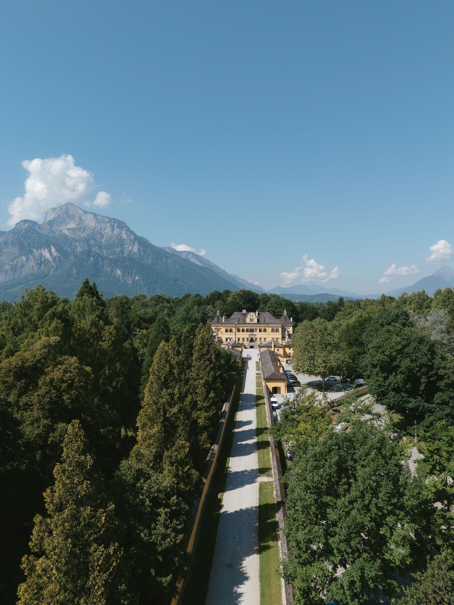 A panoramic view of Herrenchiemsee Palace's formal gardens with fountains and manicured hedges against a mountain backdrop.
