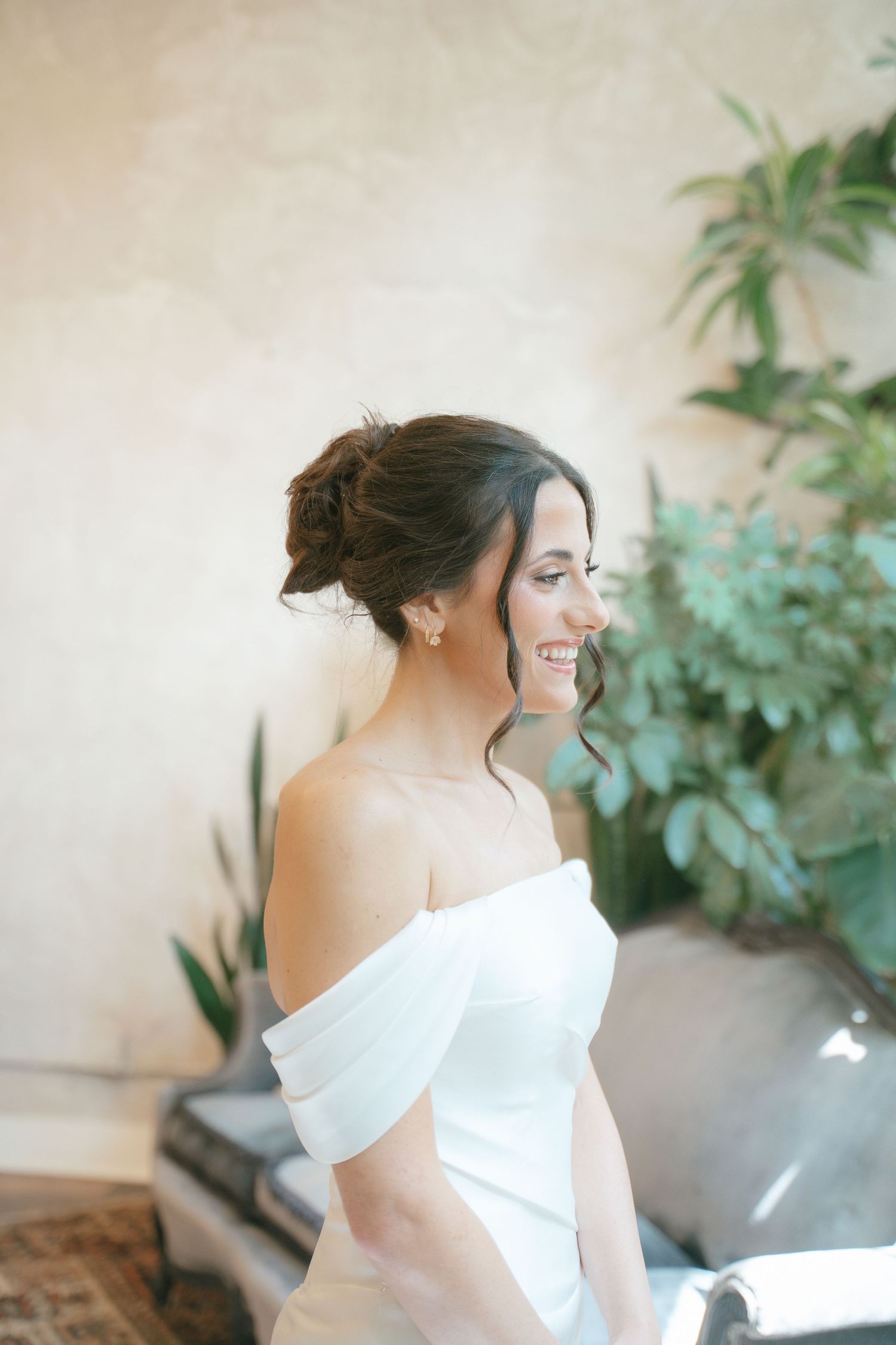 Elegant off-shoulder white wedding dress detail with soft natural lighting and greenery in background.