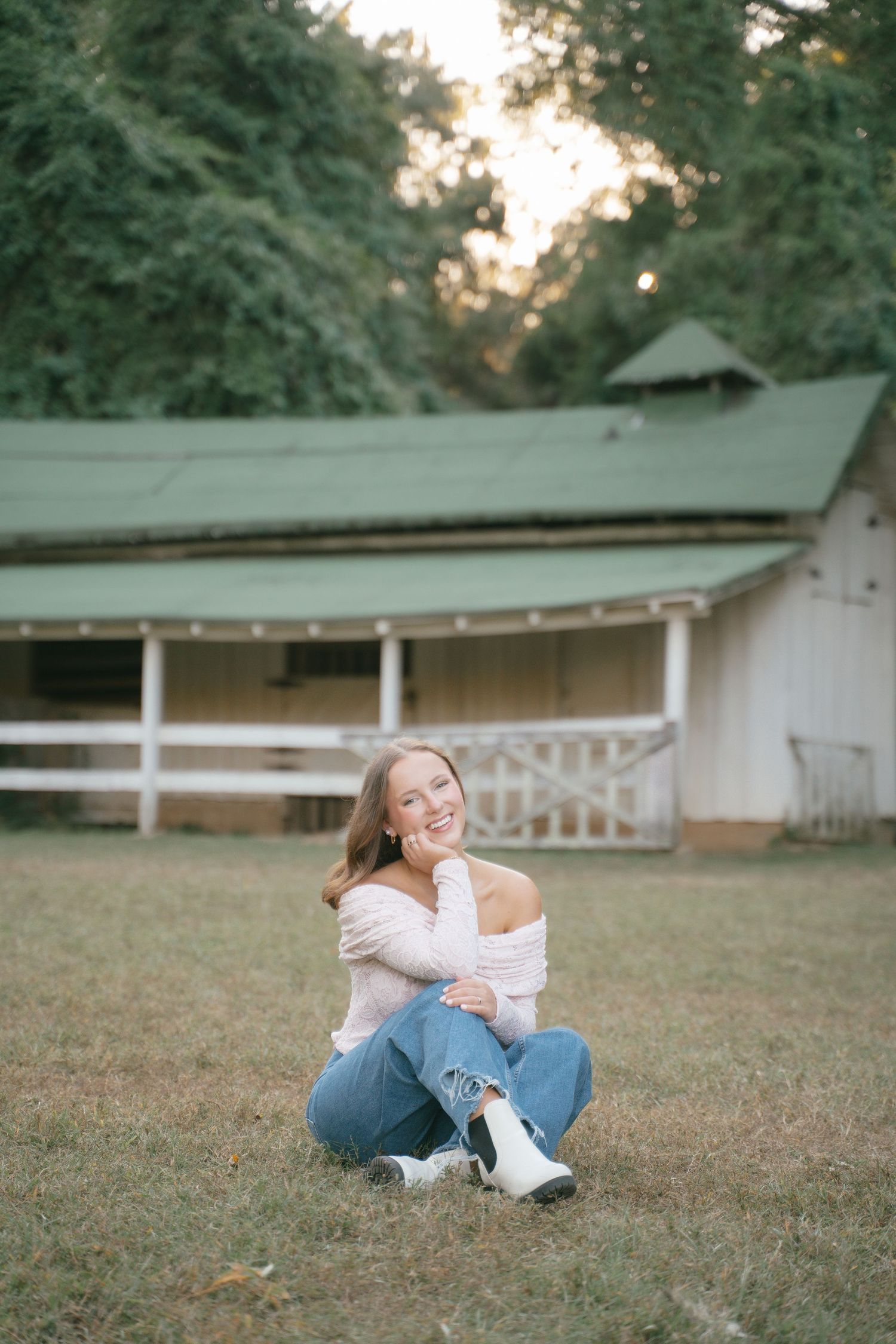 Person in casual wear relaxing on grass near rustic barn structure.