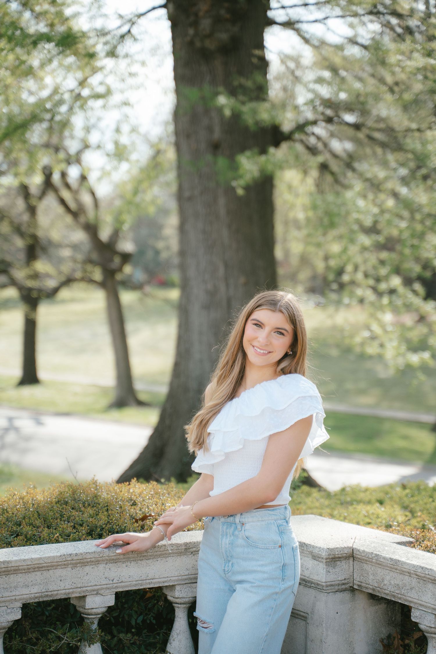 Spring senior portrait session against stone wall with blooming trees in background.