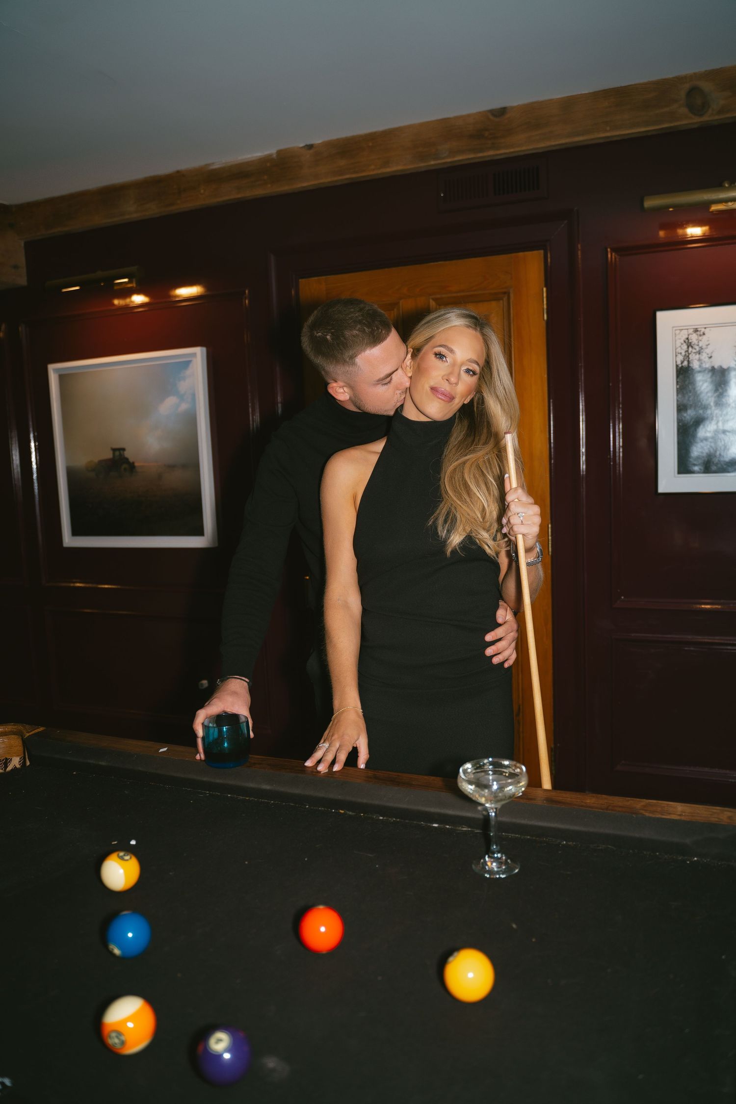A couple plays pool together in a dimly lit bar setting.