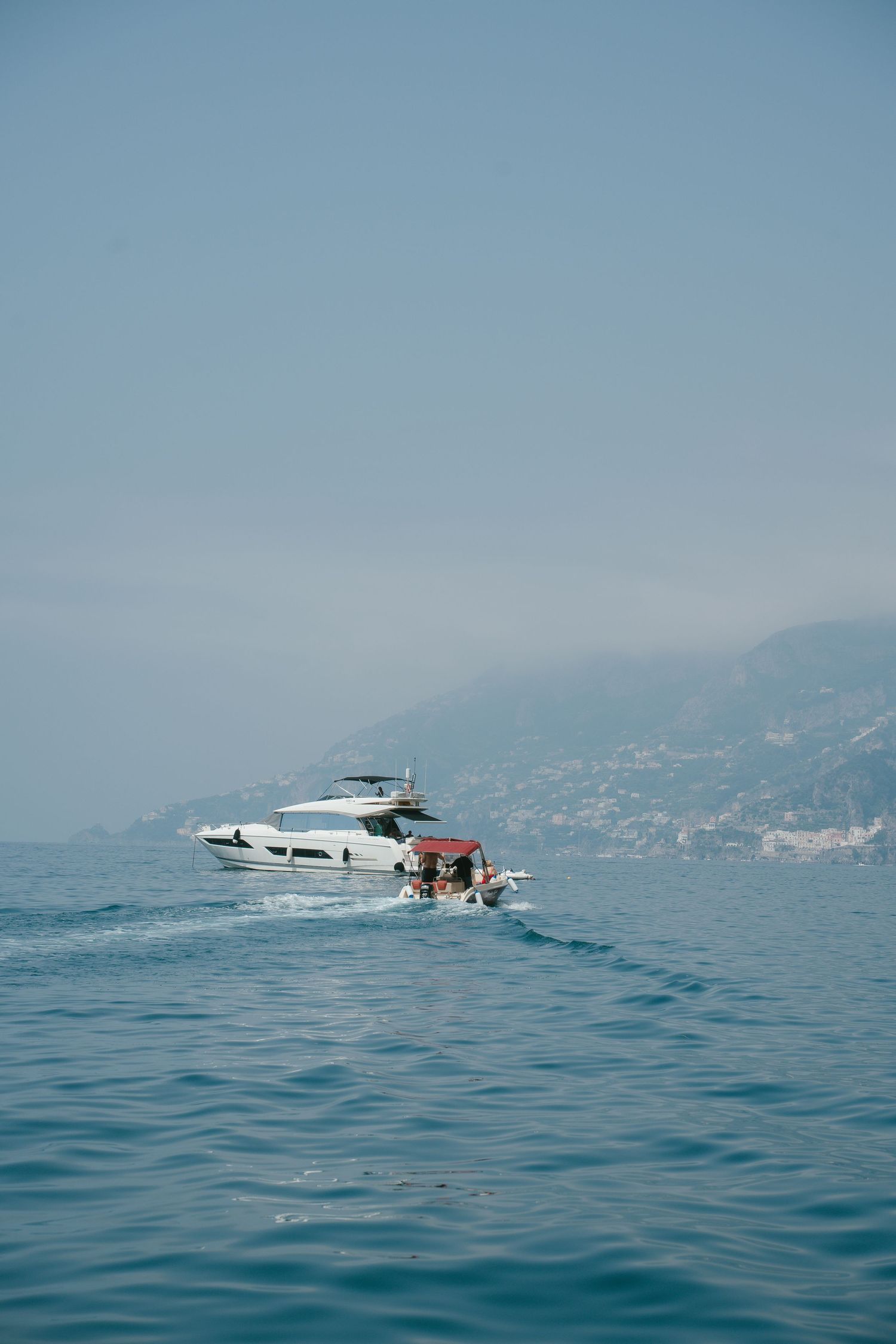 Boats cruising on calm blue Mediterranean waters with coastal mountains in background.