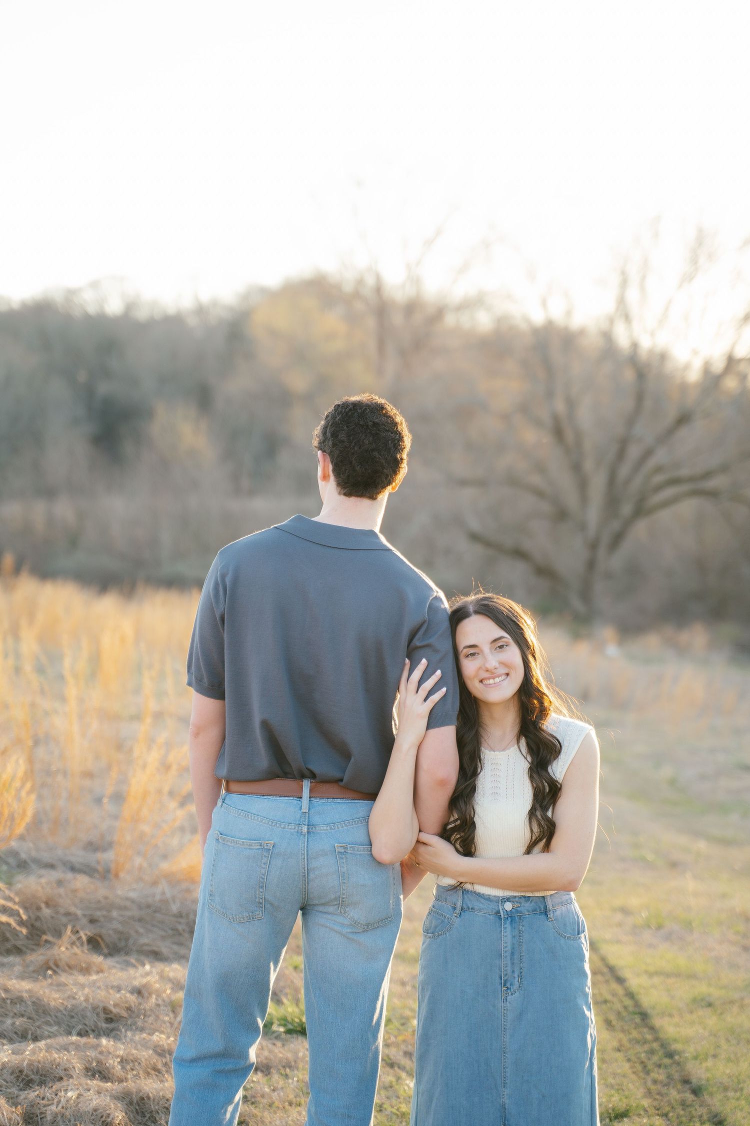 A couple walks together at sunset in casual denim and white outfits.
