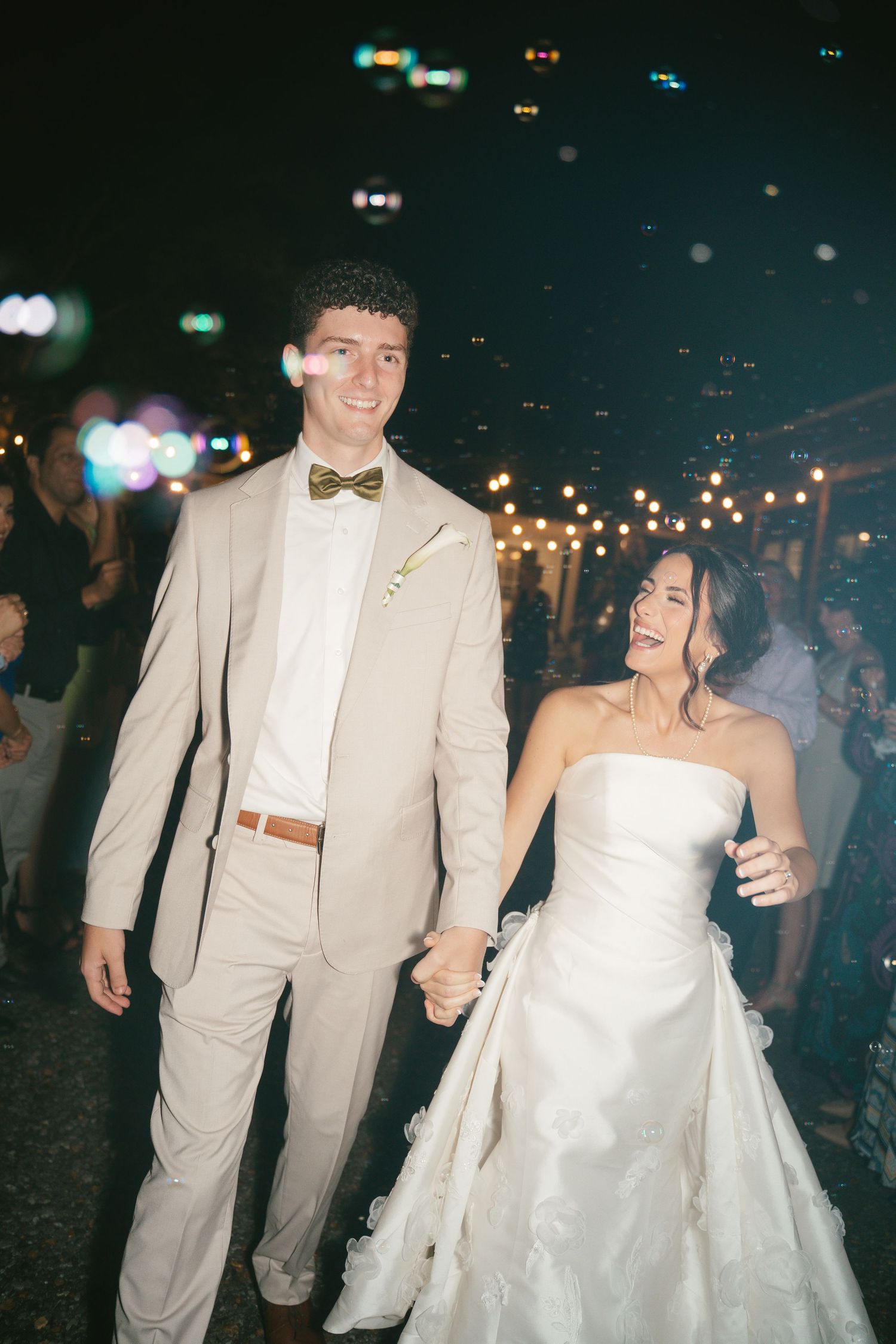 Couple in formal attire dancing under string lights at night celebration.
