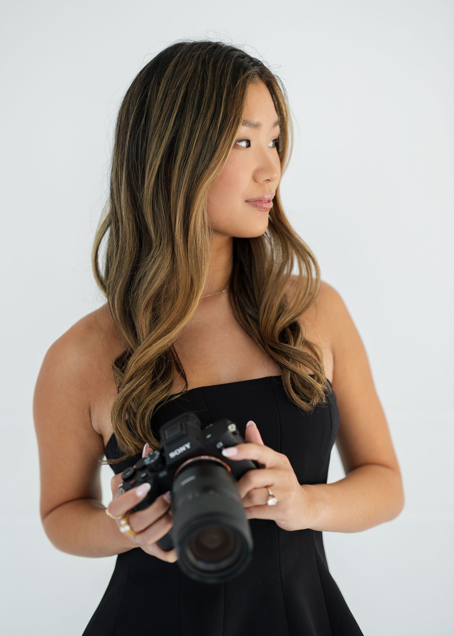 Person in black dress holding professional camera against white backdrop in sequence.