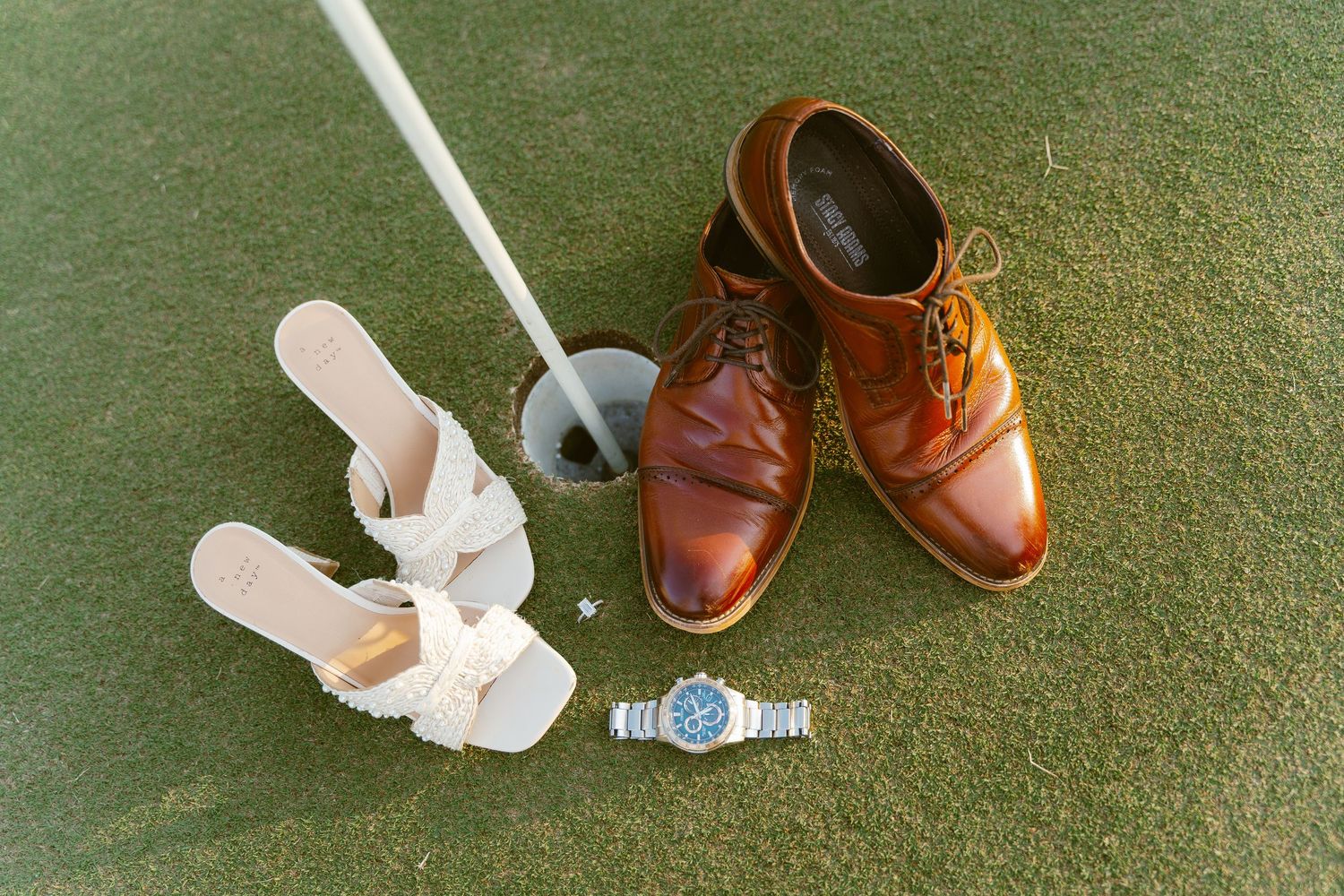 Brown leather shoes and white sneakers arranged in a row on green carpet.