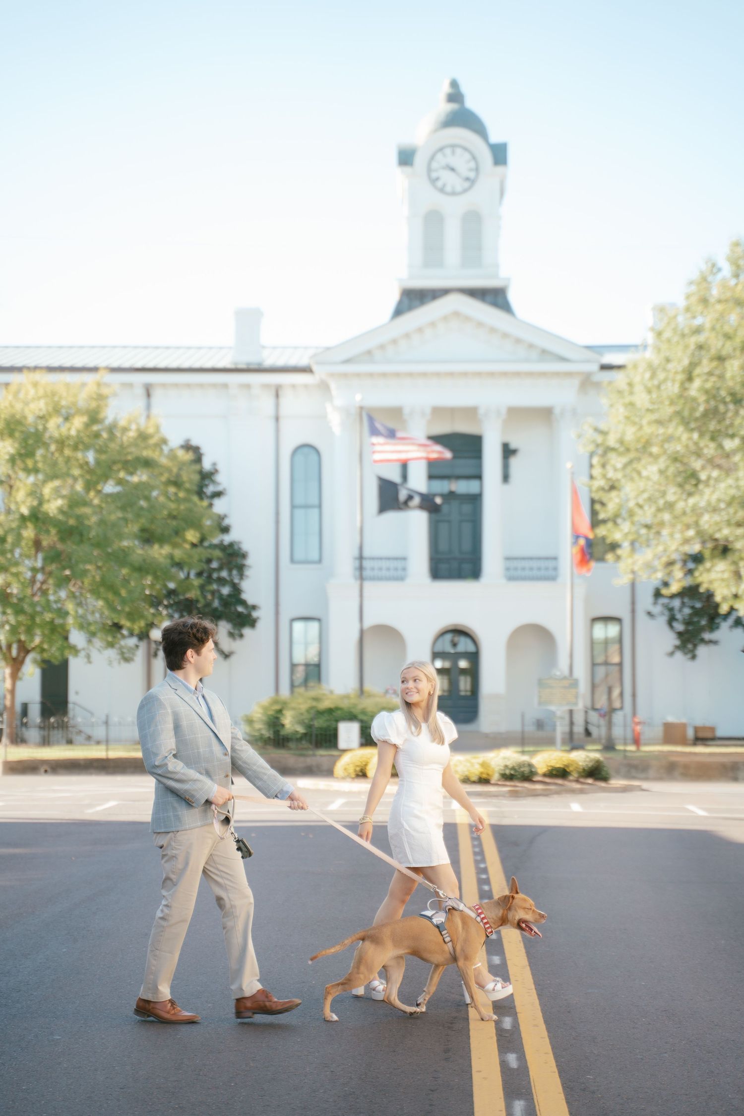 A couple dances with their golden retriever in front of a historic white church.