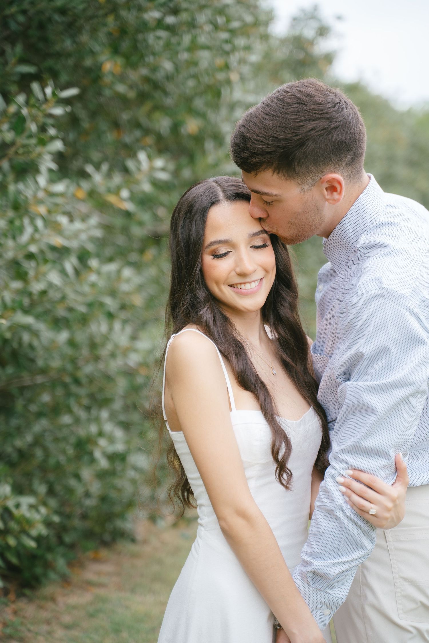 Romantic couple in white sharing intimate moment among green foliage.
