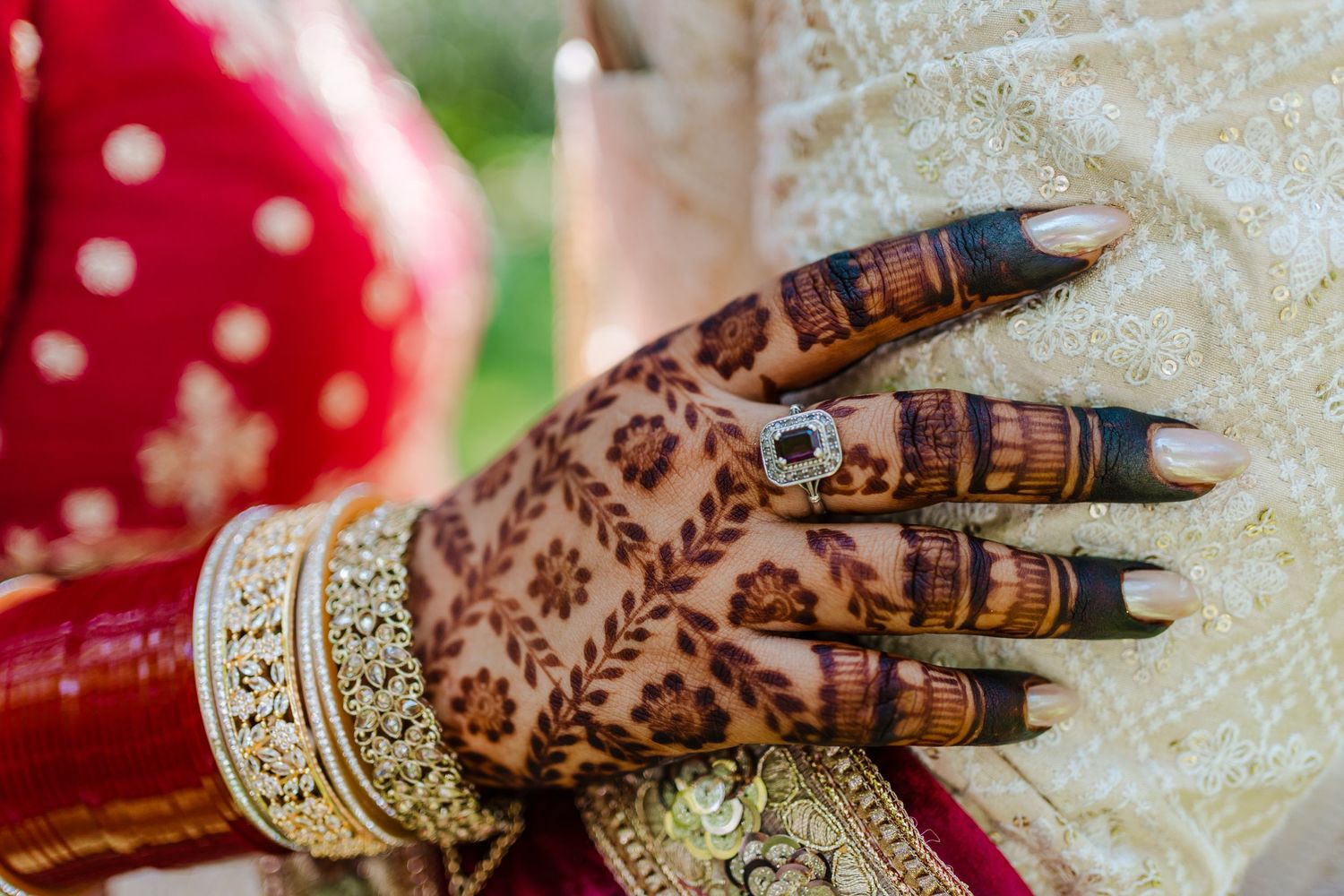 Intricate henna design on hand with gold bangles and red traditional wedding attire.