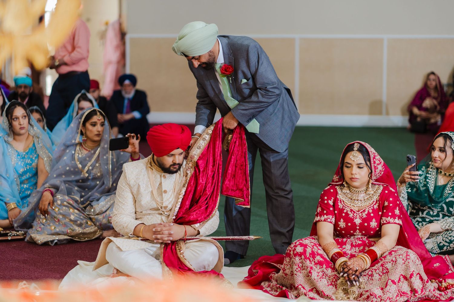 Traditional Sikh wedding ceremony in progress with guests seated on the floor during a vibrant indoor celebration.