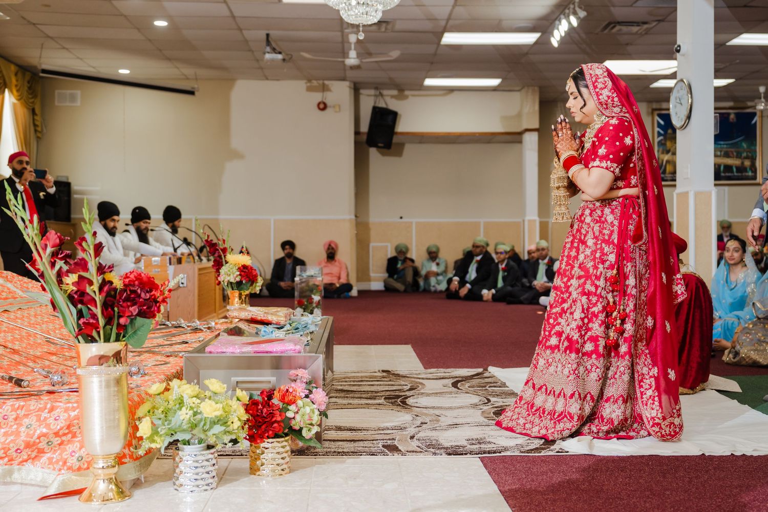 Traditional Indian wedding ceremony in a banquet hall with vibrant red decor and floral arrangements.
