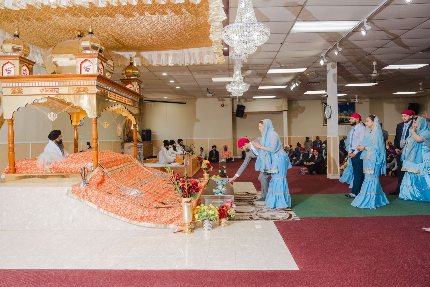 Traditional Sikh wedding ceremony taking place in decorated temple hall with ornate altar.