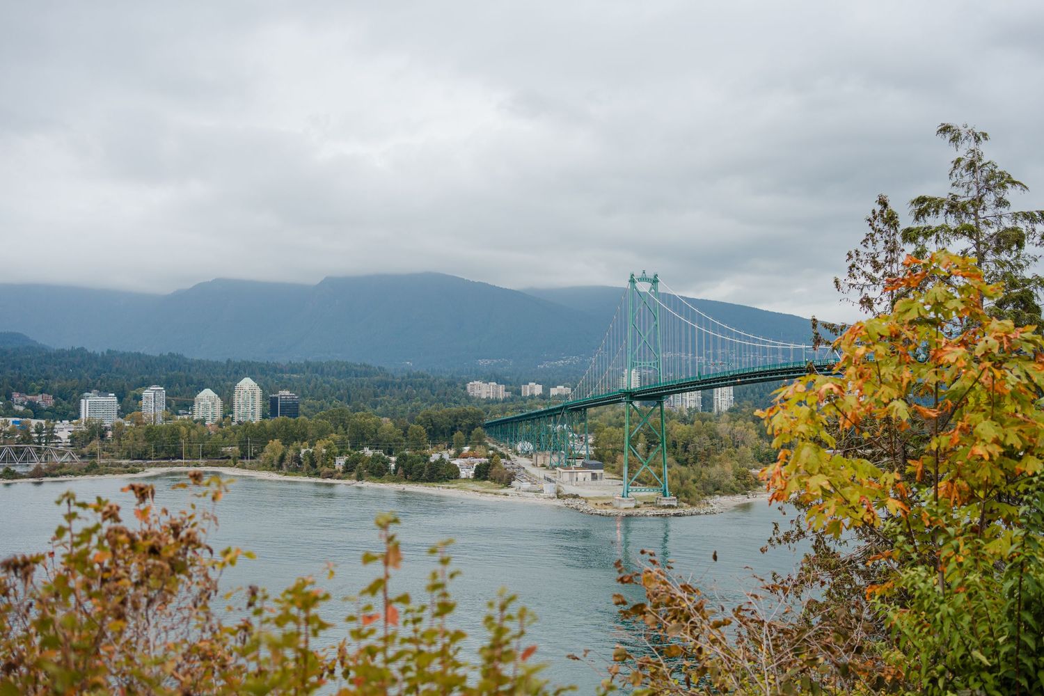 Lions Gate Bridge spanning across water with mountains and autumn foliage in Vancouver.
