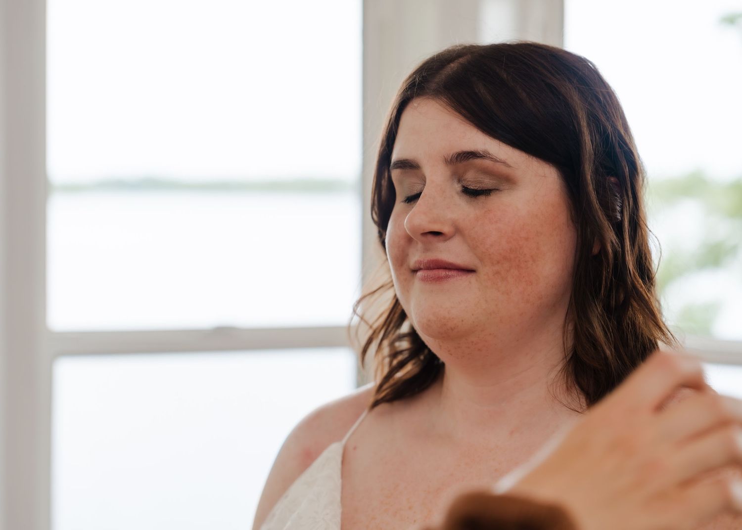 Woman with dark wavy hair and natural makeup smiles with closed eyes in a serene pose.