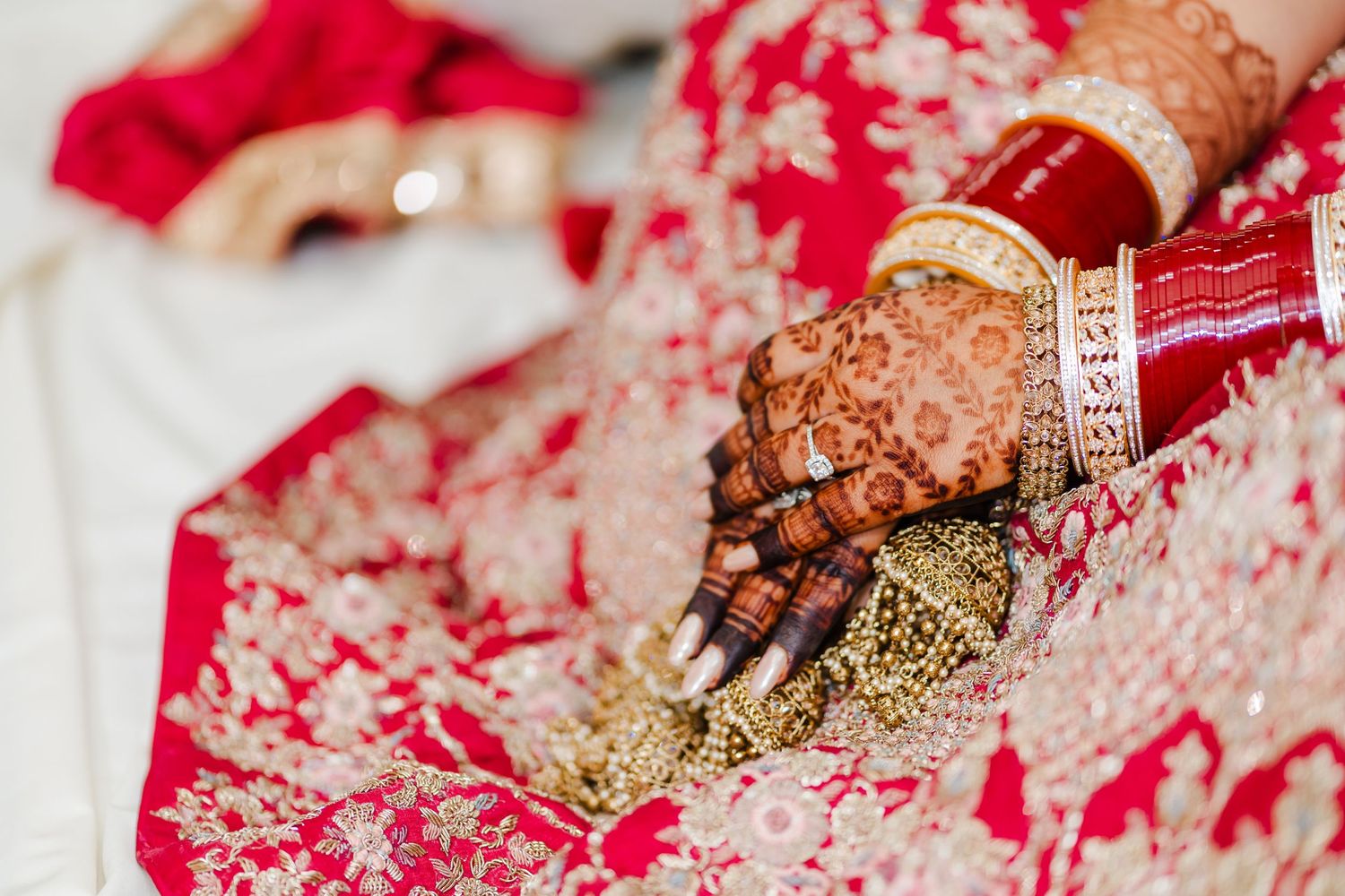 Close-up detail of traditional Indian bridal mehndi and bangles on hands with red and gold wedding attire.