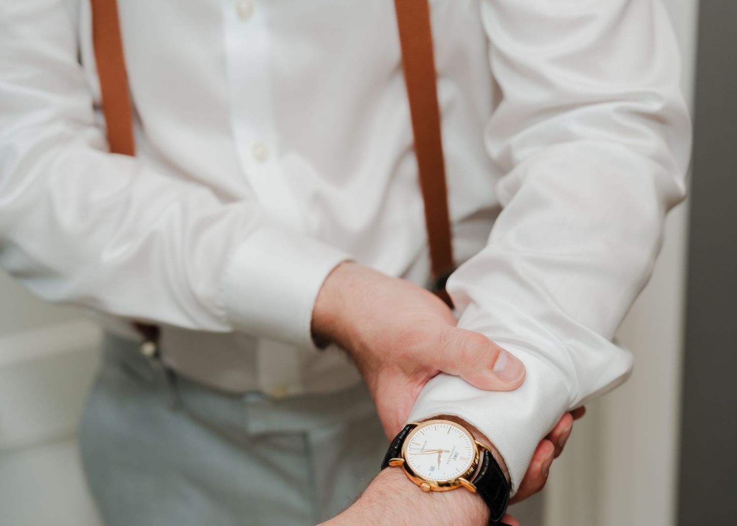 Close-up of a groom's wrist showing a watch and brown leather suspenders with white shirt.