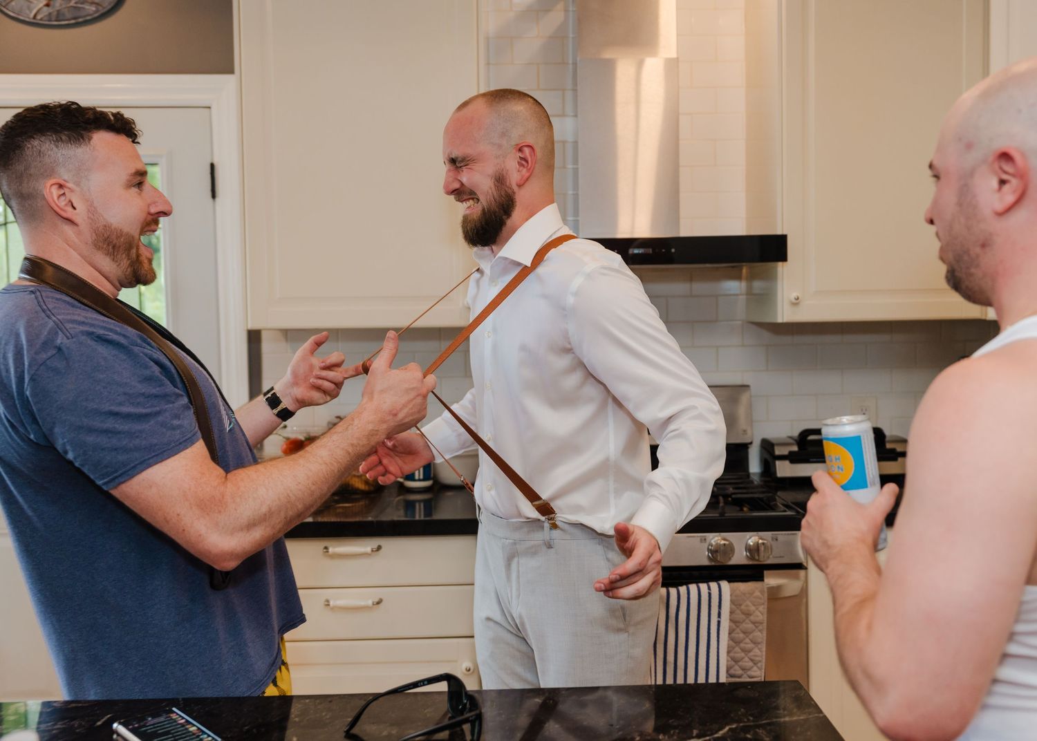 Three people having an animated conversation in a modern white kitchen.
