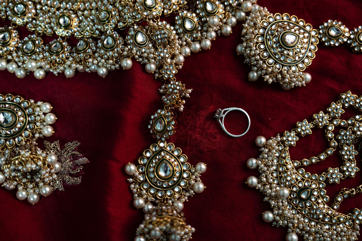 Ornate bridal jewelry with pearls and crystals displayed on red velvet with wedding rings.